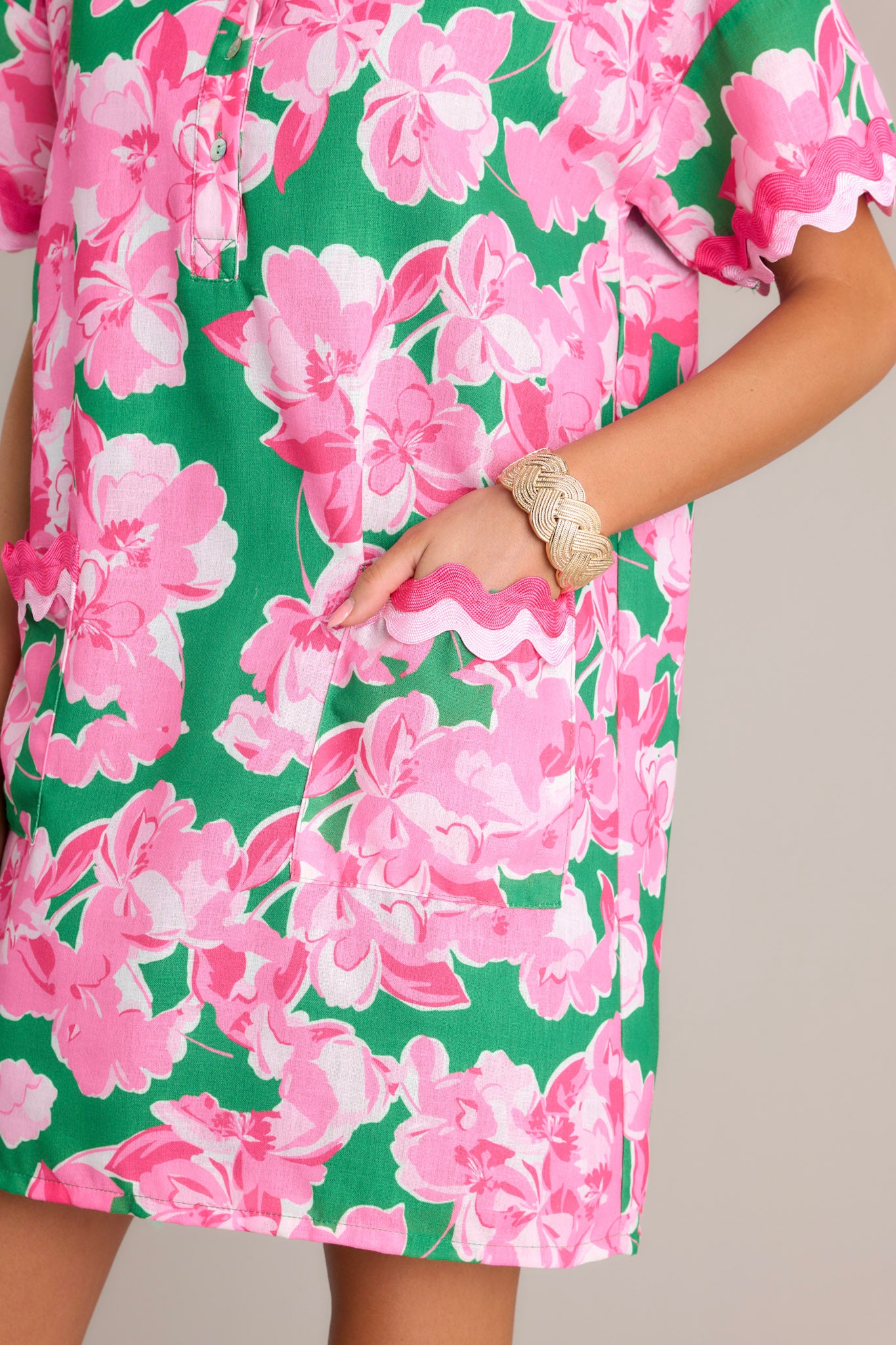 Close-up of the green floral mini dress showing the collared neckline, functional half button front, and functional front pockets with ricrac detailing.