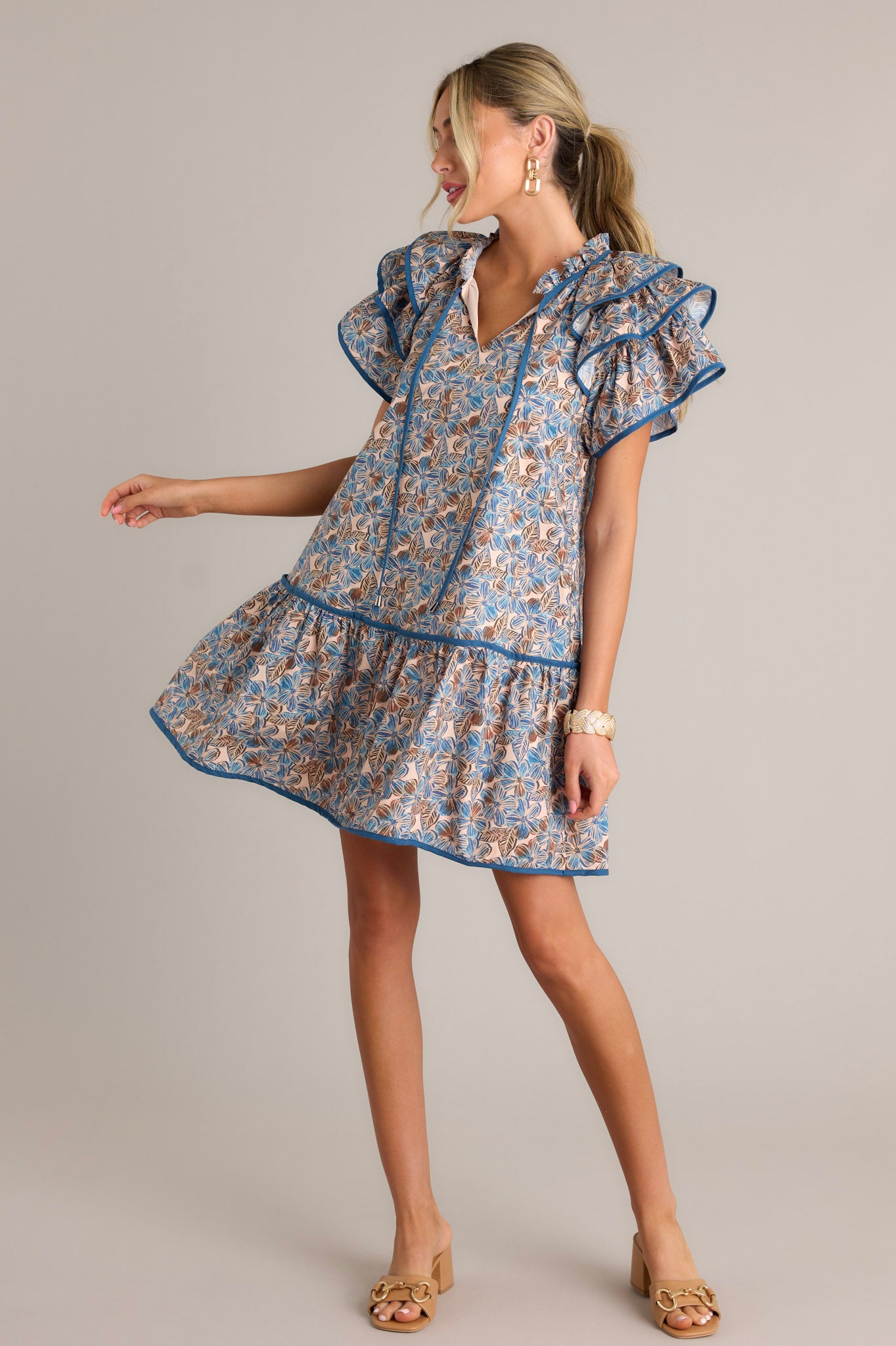 This blue floral mini dress features a ruffled v-neckline with a self-tie feature, a relaxed fit, functional hip pockets, a single tier, and ruffled short sleeves.