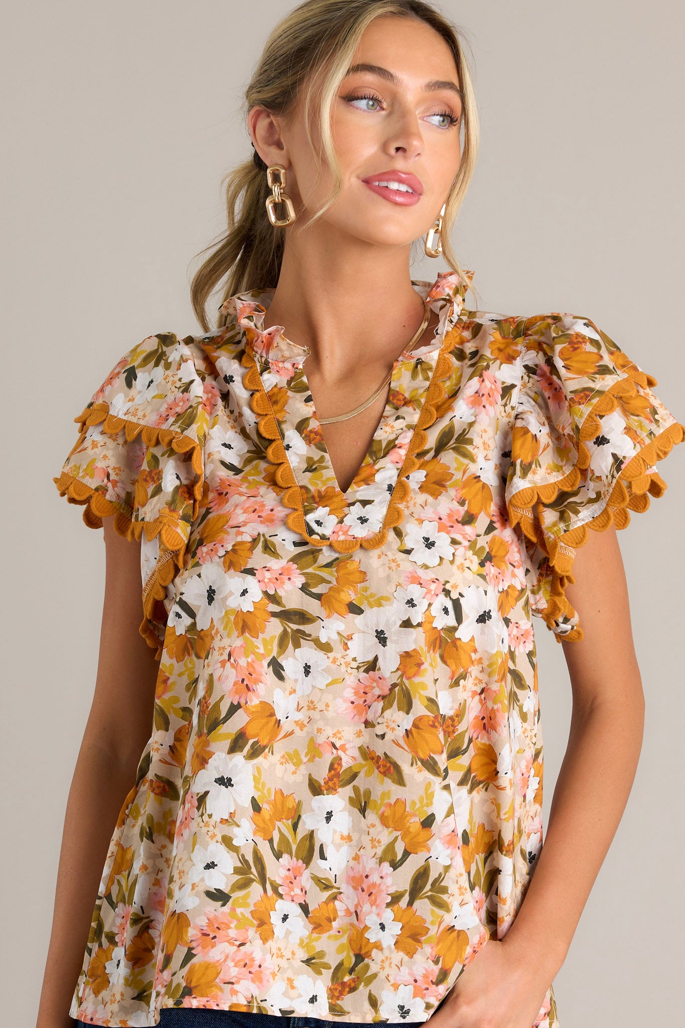 Front angled view of a yellow top featuring a ruffled v-neckline, scalloped detailing, a lightweight material, and layered scalloped short sleeves