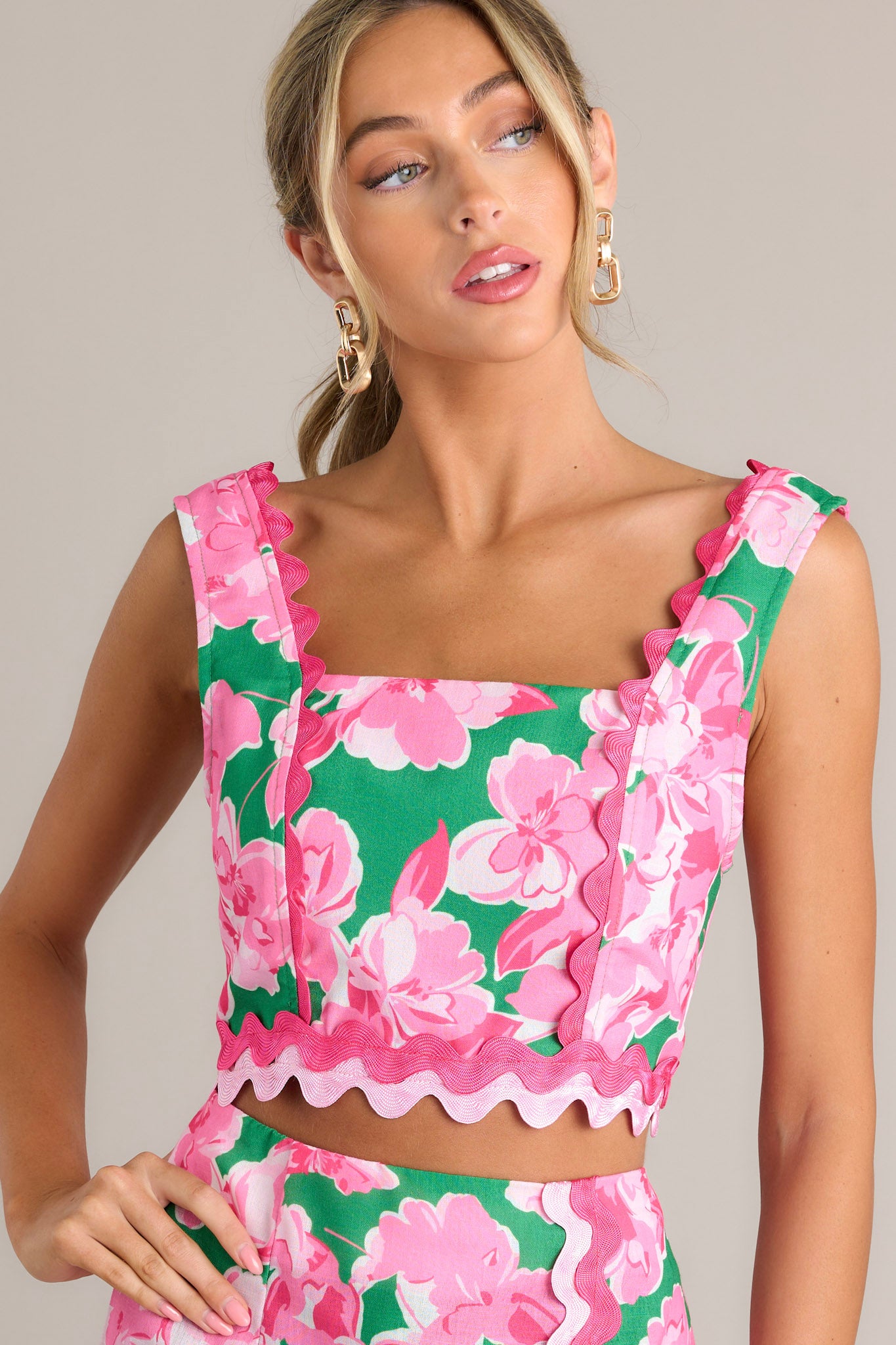 This green floral crop top features a square neckline, thick straps, a smocked back insert, a zipper, ricrac detailing throughout, and a cropped hemline.