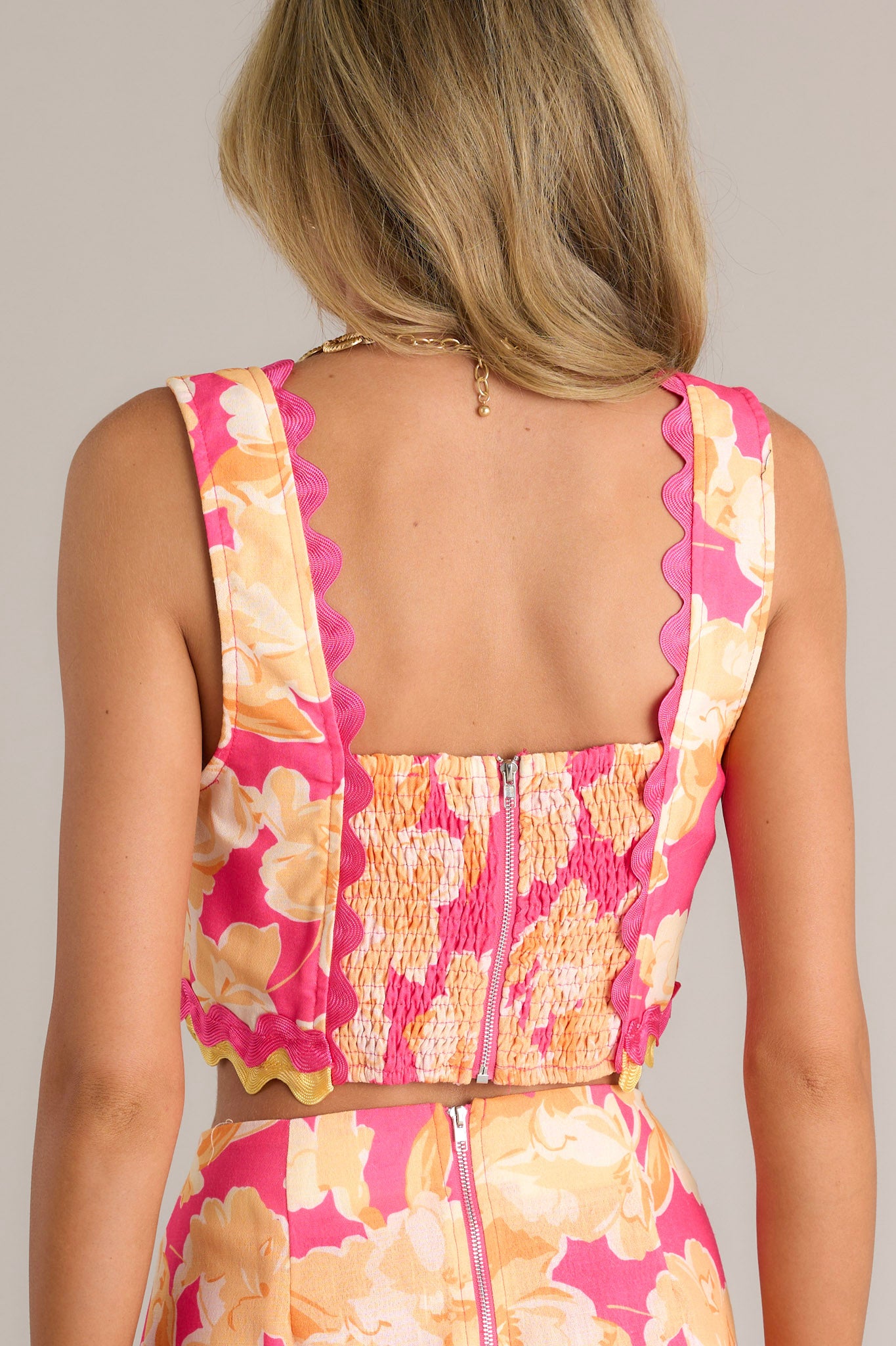 Back view of a pink floral crop top highlighting the smocked back insert, zipper, and overall fit.