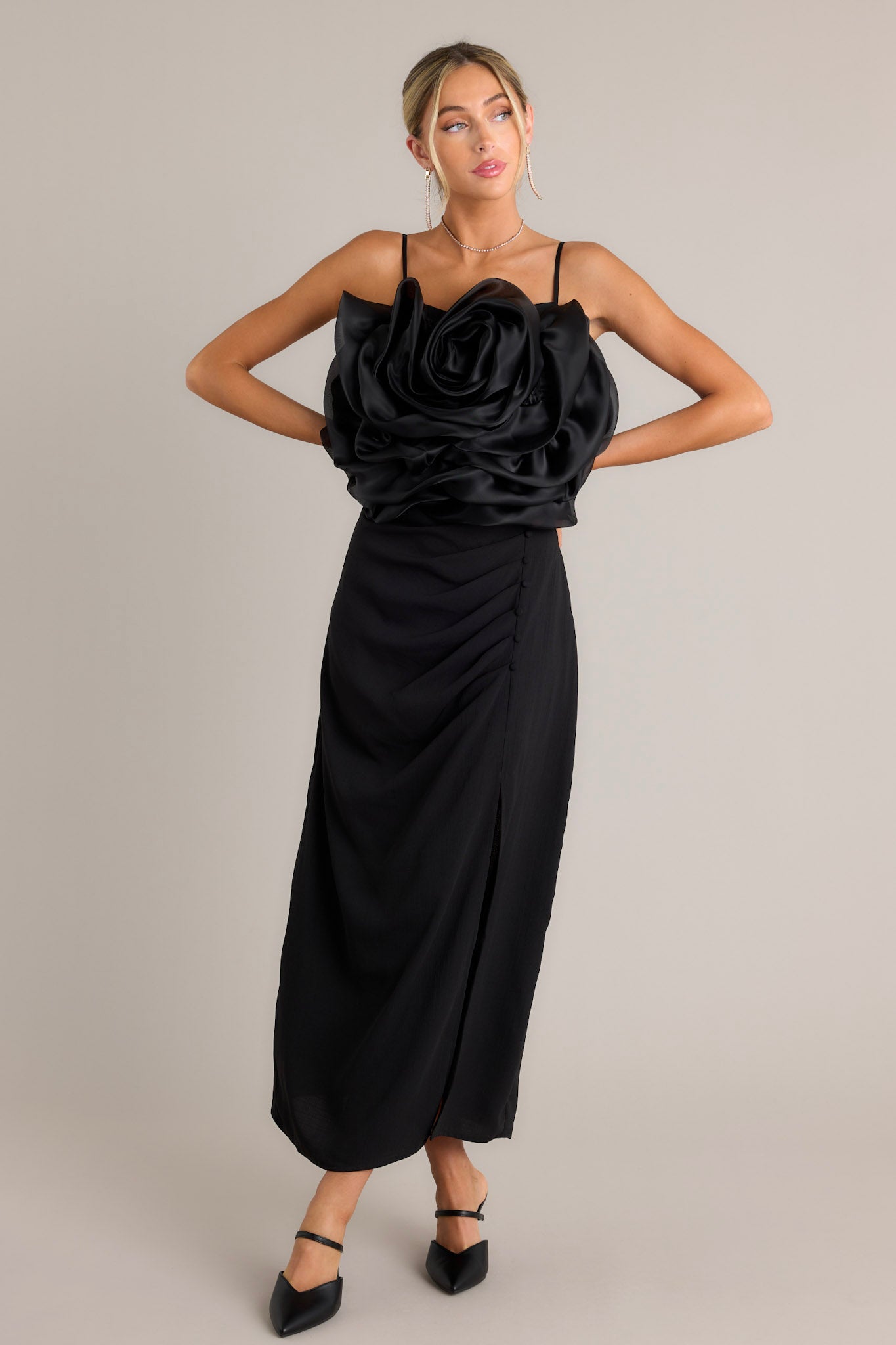 Full length view of a black crop top with a square neckline, thin and stretchy adjustable straps, a fully smocked back, a large 3-D flower, and a cropped hemline
