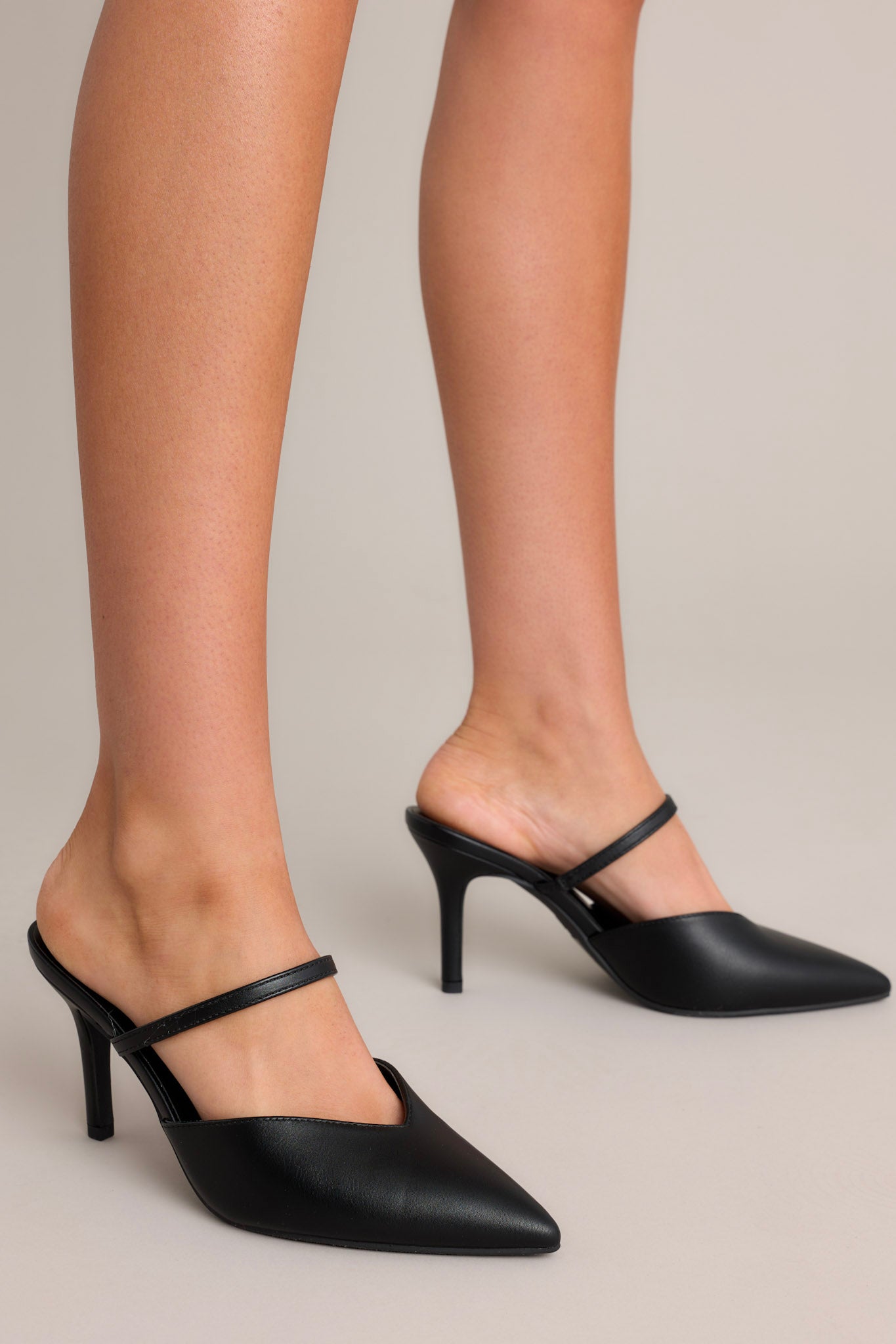 Side view of these heels that feature a pointed closed toe design, a strap over the top of the foot, and a short heel.