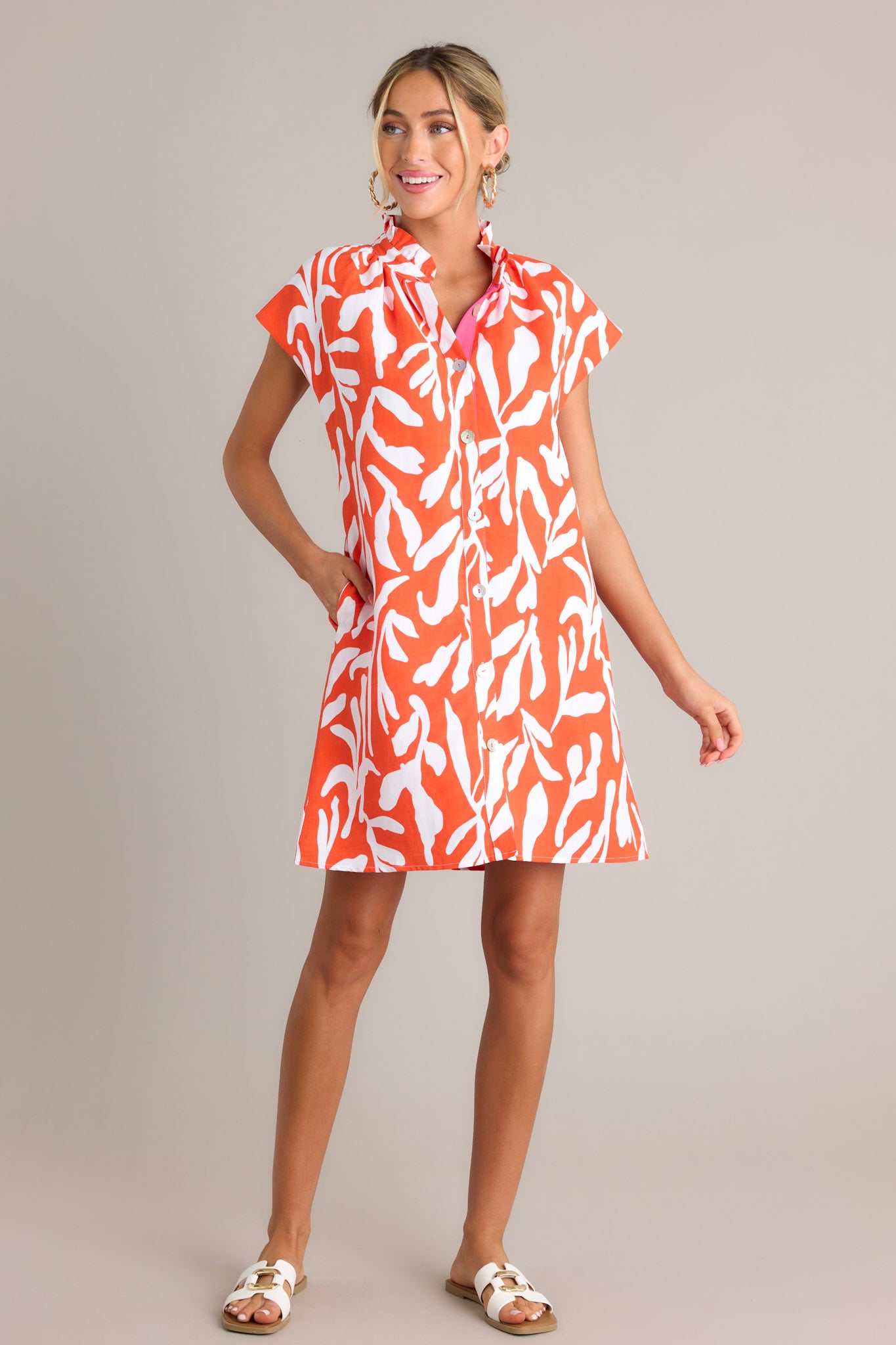 This red orange dress features a ruffled collar, caped short sleeves, Functional buttons, a fun abstract print, and functional hip pockets.