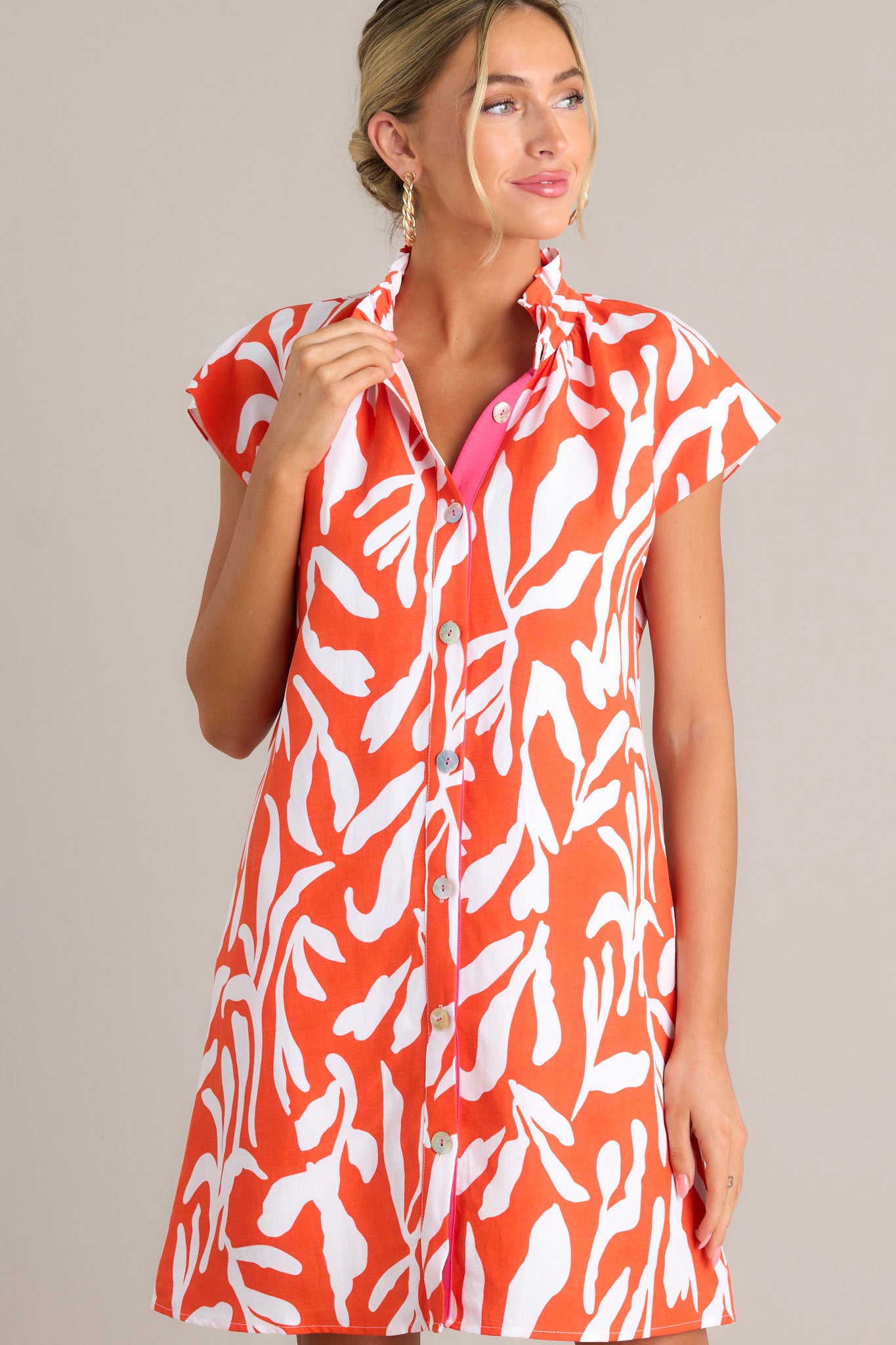 Full length view of a red orange dress with a ruffled collar, caped short sleeves, functional buttons, a fun abstract print, and functional hip pockets