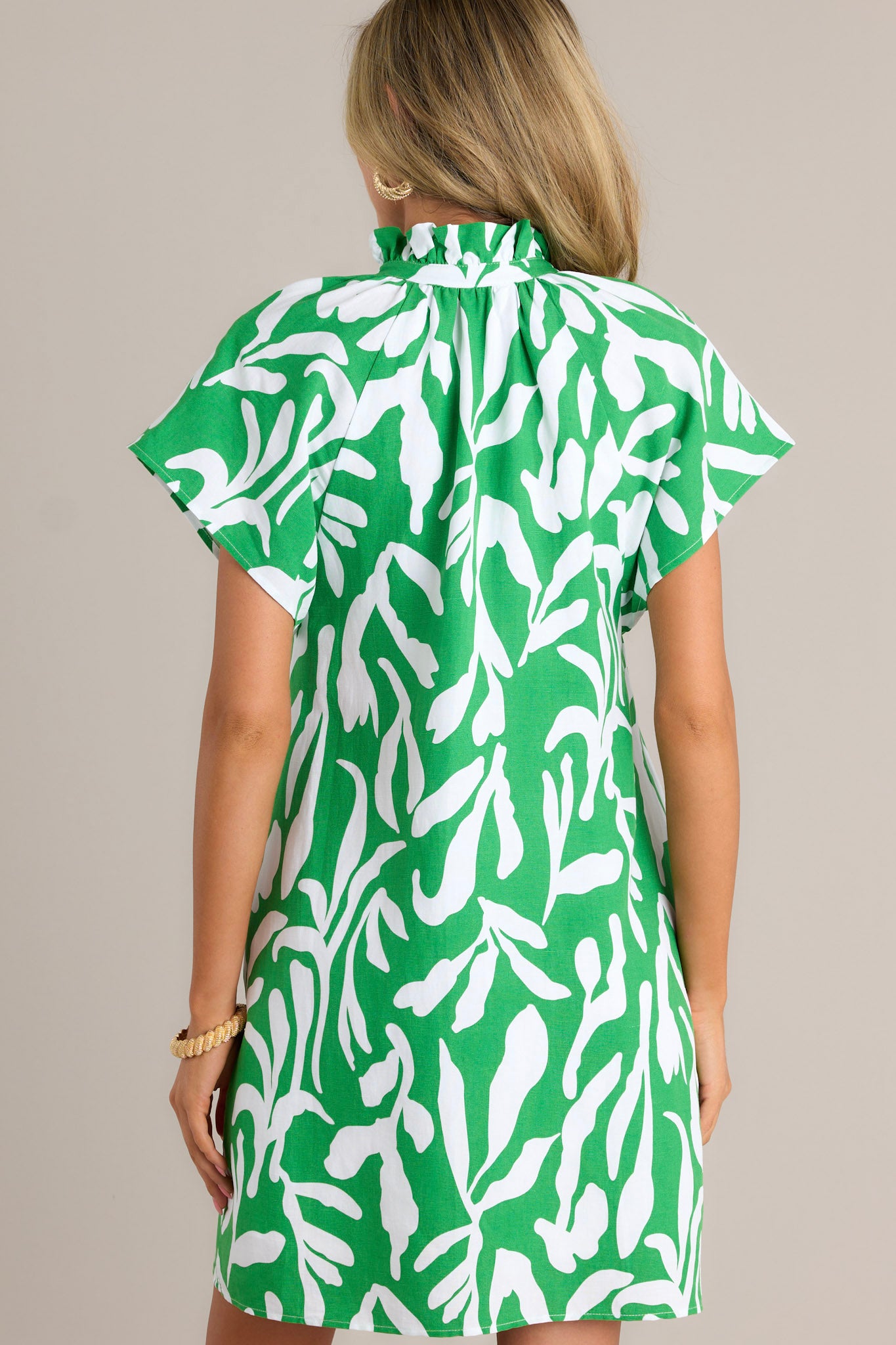 Back view of a green floral mini dress highlighting the unique floral design, short flutter sleeves, and overall fit.