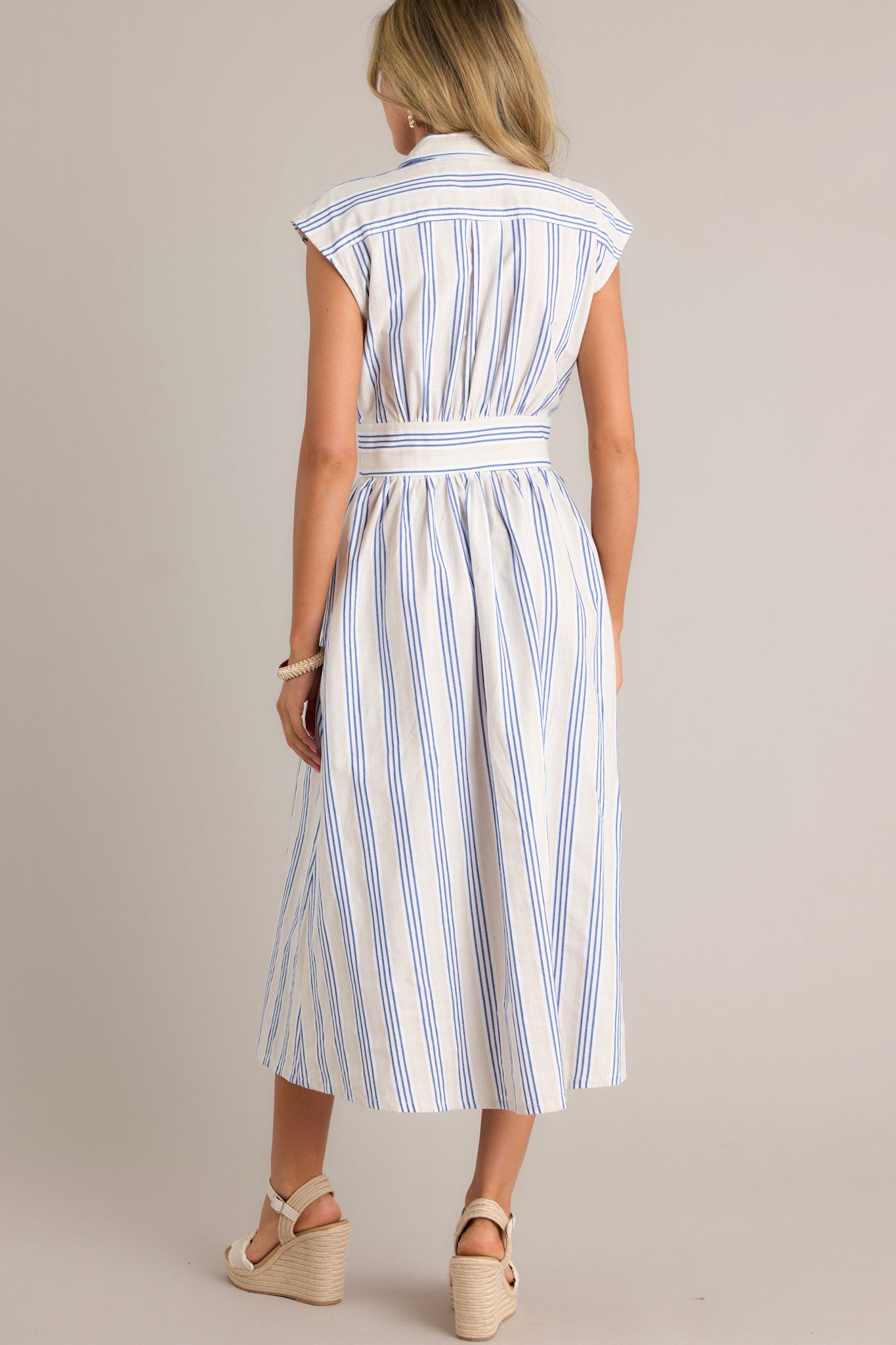 Back view of a blue stripe midi dress highlighting the overall fit, beige and blue stripe pattern, and flowing silhouette.