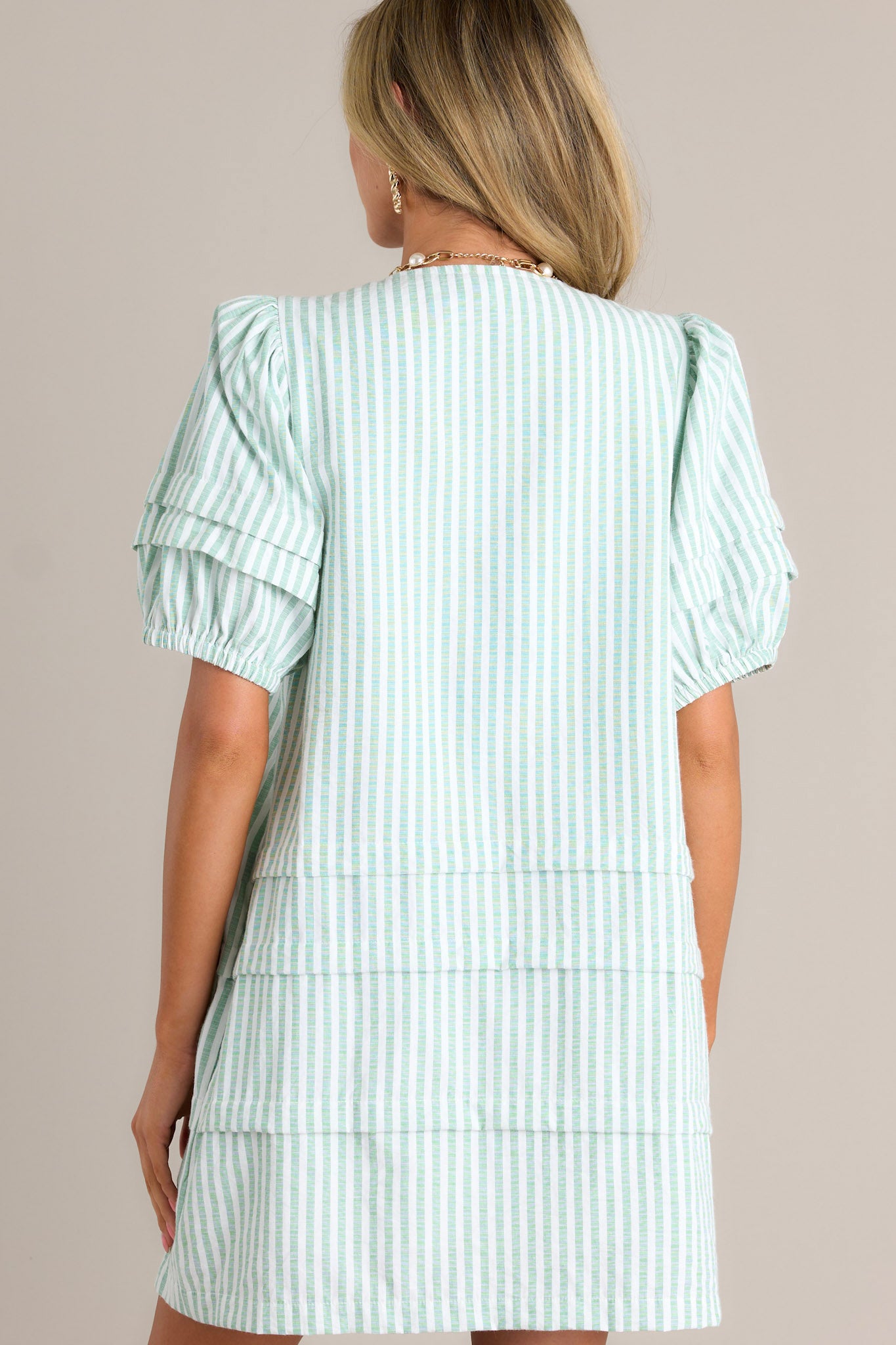 Back view of a mint green mini dress highlighting the slight shoulder enhancement, tiered design, and overall fit.