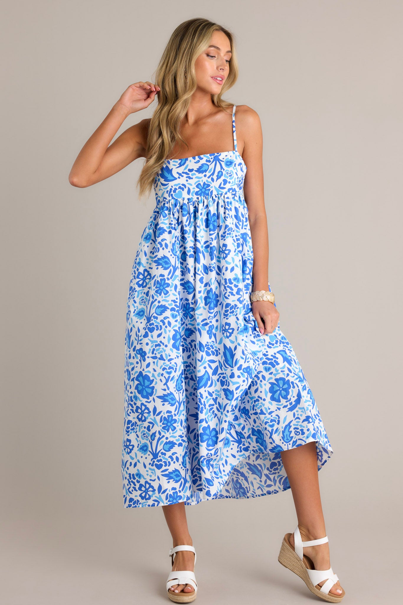 Front view of a blue floral maxi dress featuring a square neckline, thin adjustable straps, a self-tie back feature, a small cutout detail, functional hip pockets, and a flowing silhouette.