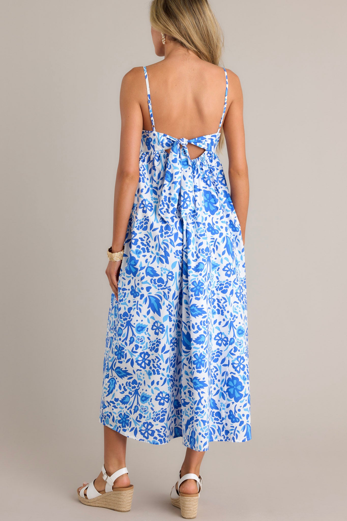 Back view of a blue floral maxi dress highlighting the self-tie back feature, small cutout detail, and overall fit.