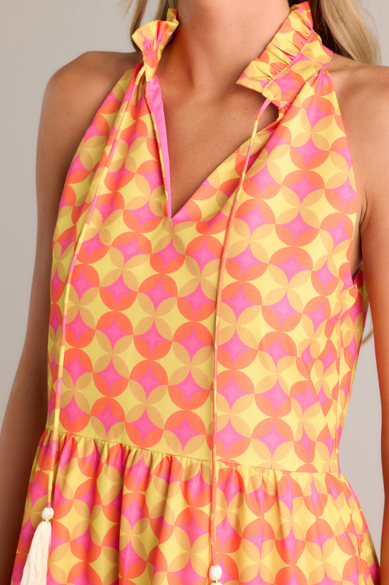 Close-up of the orange mini dress showing the ruffled v-neckline, self-tie neck feature, and unique pattern.