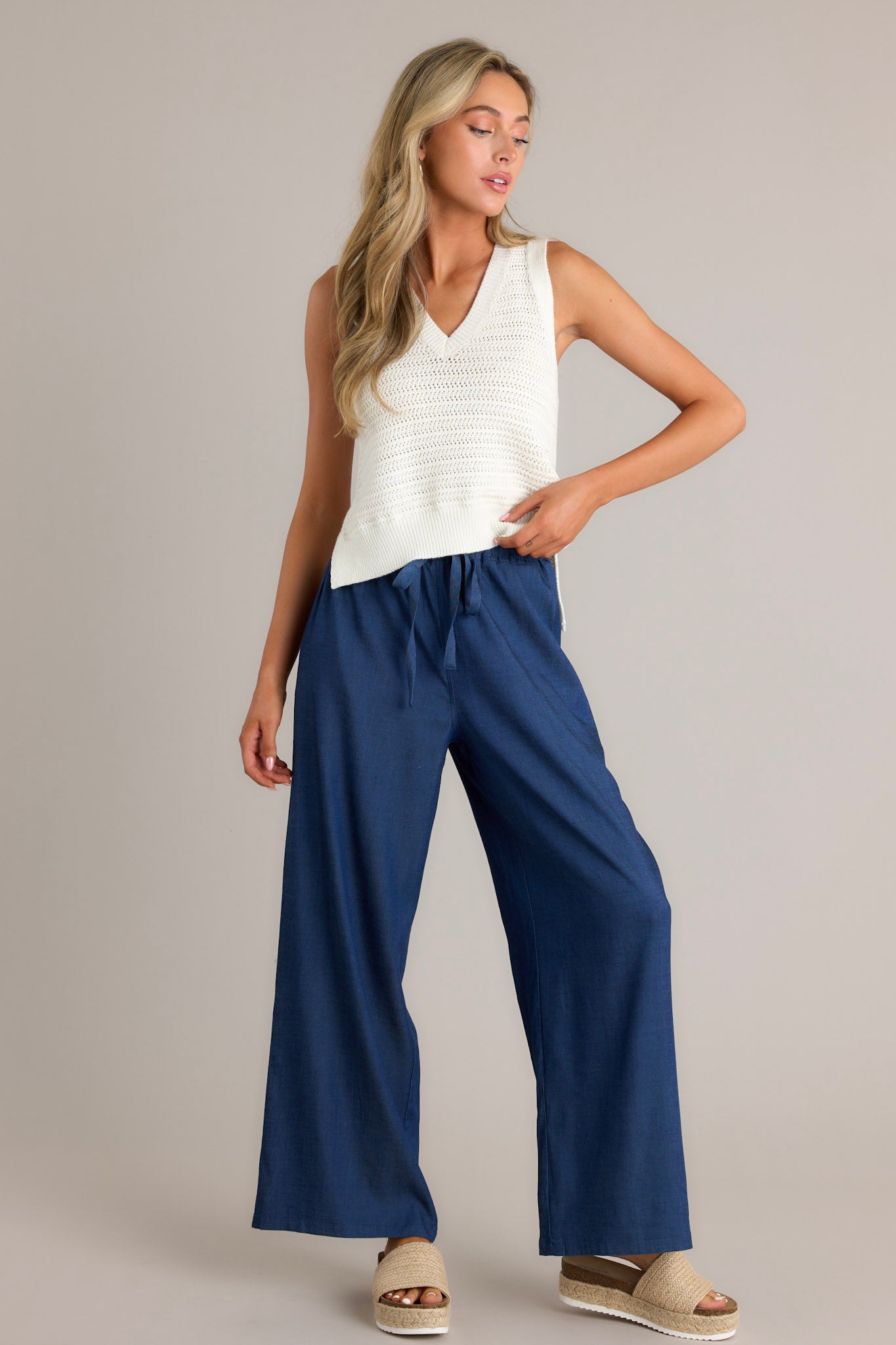 Front angled view of dark chambray pants featuring a high waisted design, an elastic waistband, a self-tie drawstring, functional hip pockets, and a wide leg