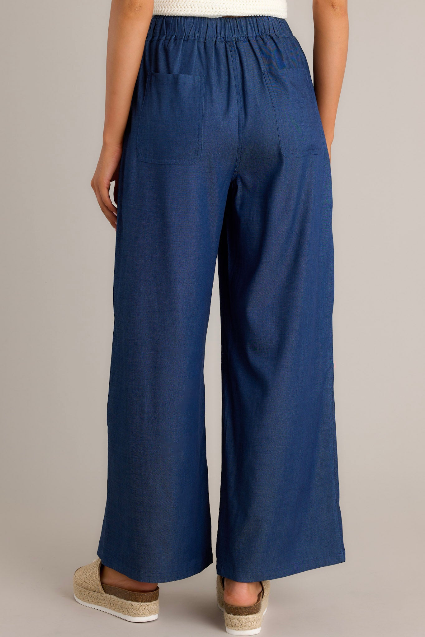 Back view of dark chambray pants highlighting the high waisted design, elastic waistband, and wide leg.