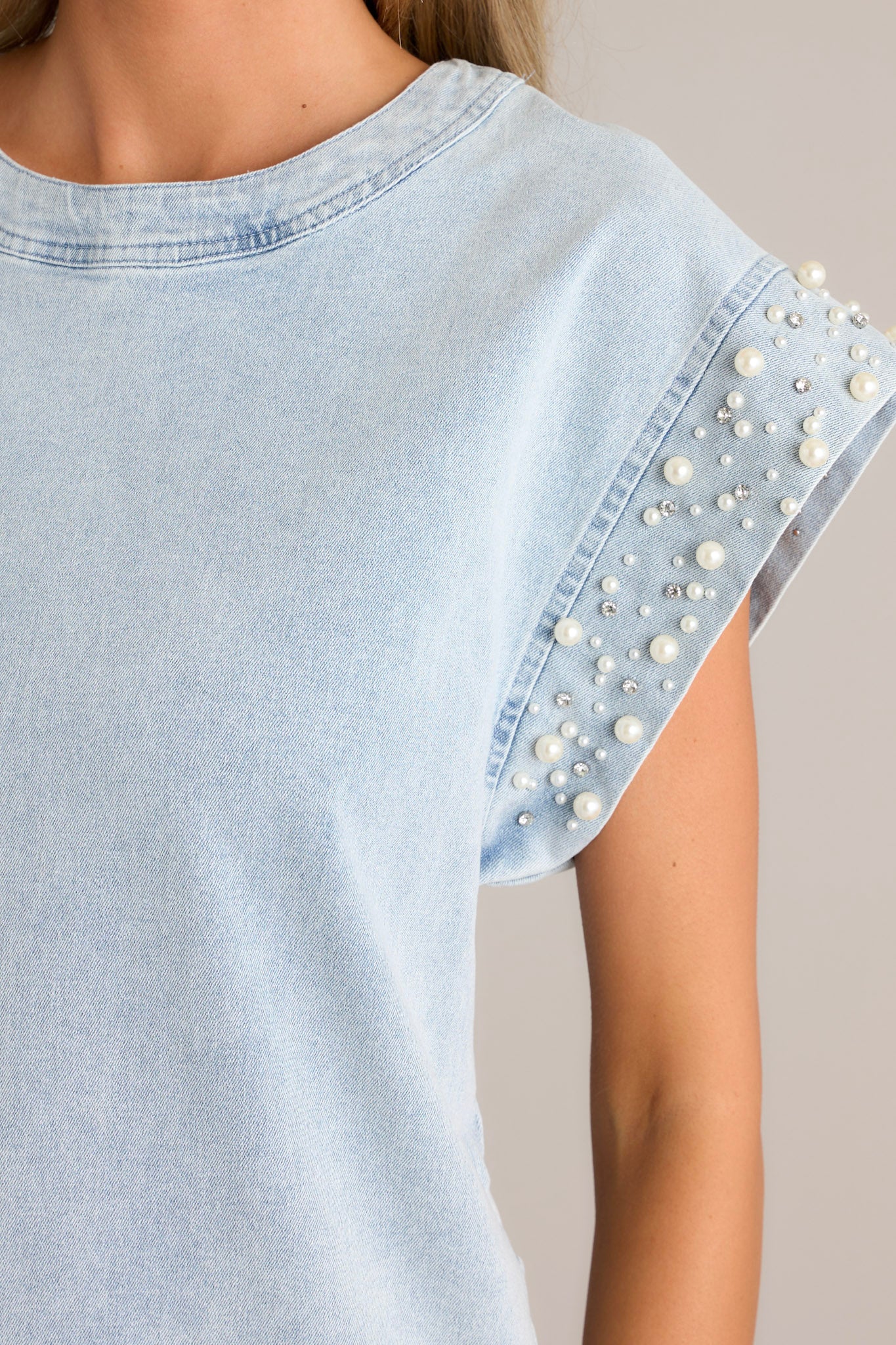 Close-up of the light wash mini dress showing the rounded neckline, denim material, and the pearl & rhinestone embellishments on the wide cap sleeves.