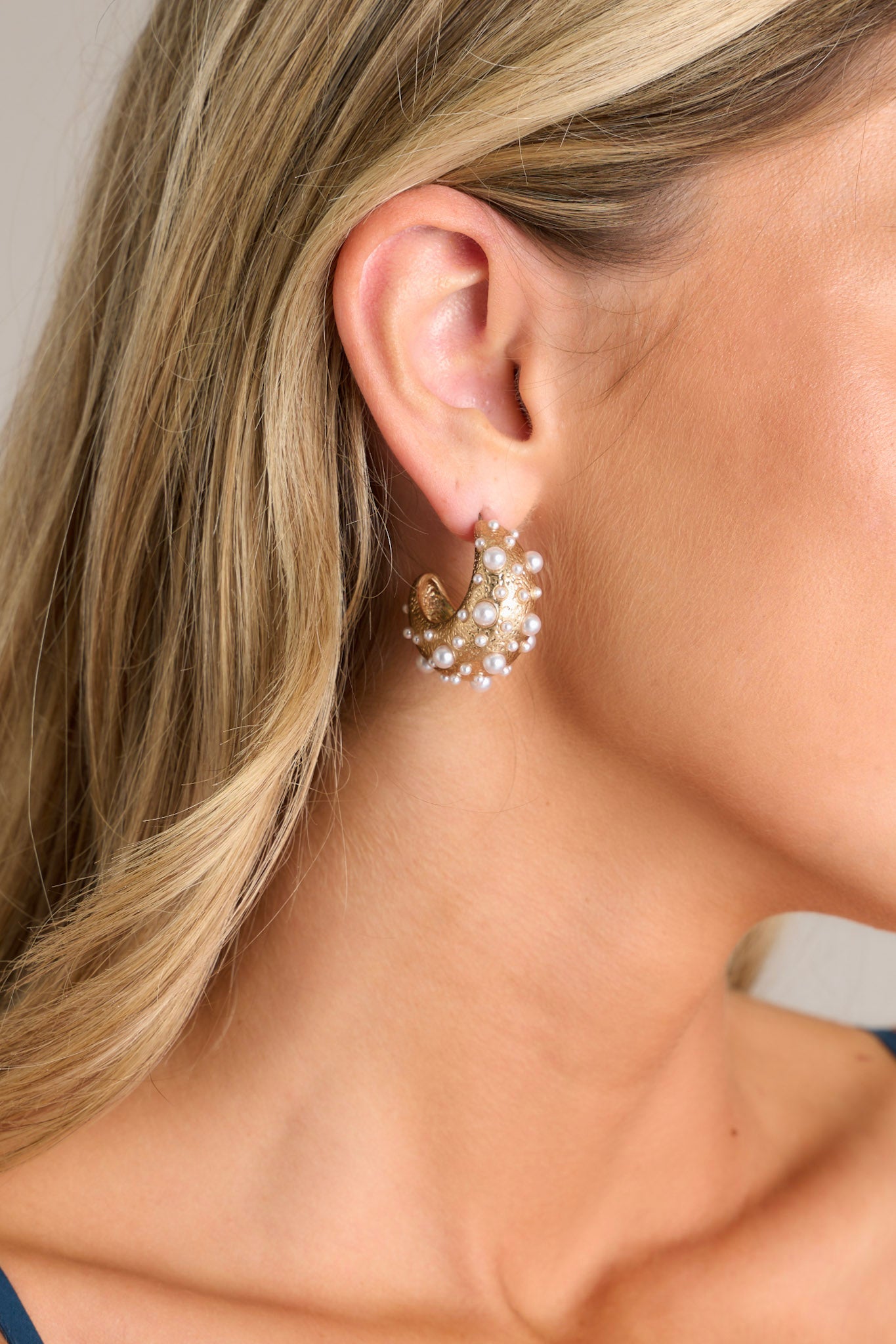 Close-up of these hoop earrings featuring a textured gold material, adorned with faux pearls varying in size, a wide design, and secure post backings.