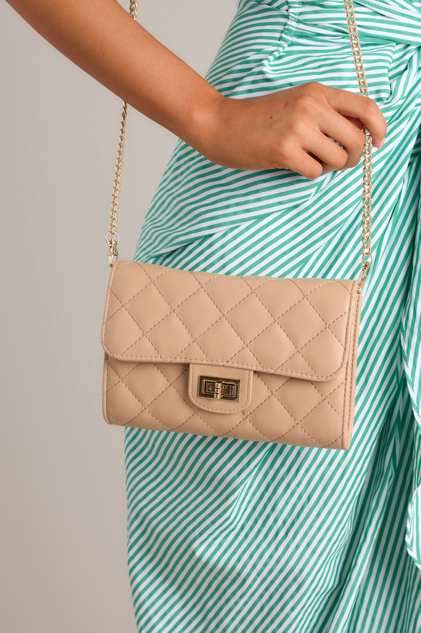 Close-up of a beige quilted crossbody bag with a gold chain strap and a front turn-lock closure.