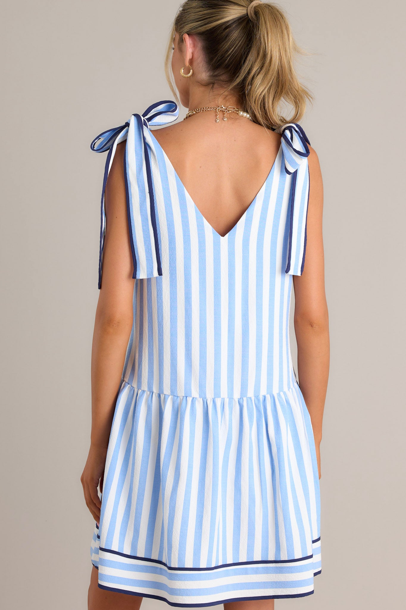 Back view of a blue mini dress highlighting the faux self-tie straps, blue & white vertical stripes, and the light & flowy material.