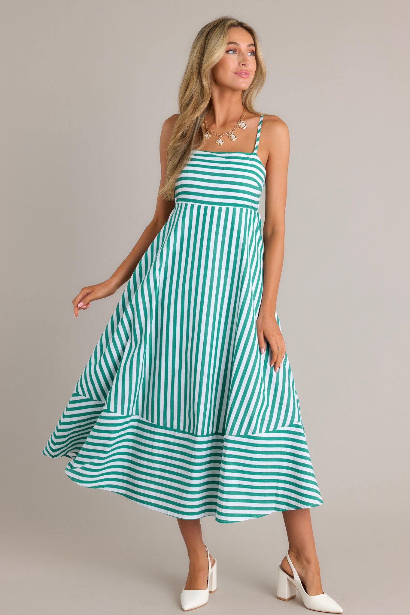 This green stripe midi dress features a square neckline, thin adjustable straps, a smocked back insert, functional hip pockets, and horizontal & vertical stripes.