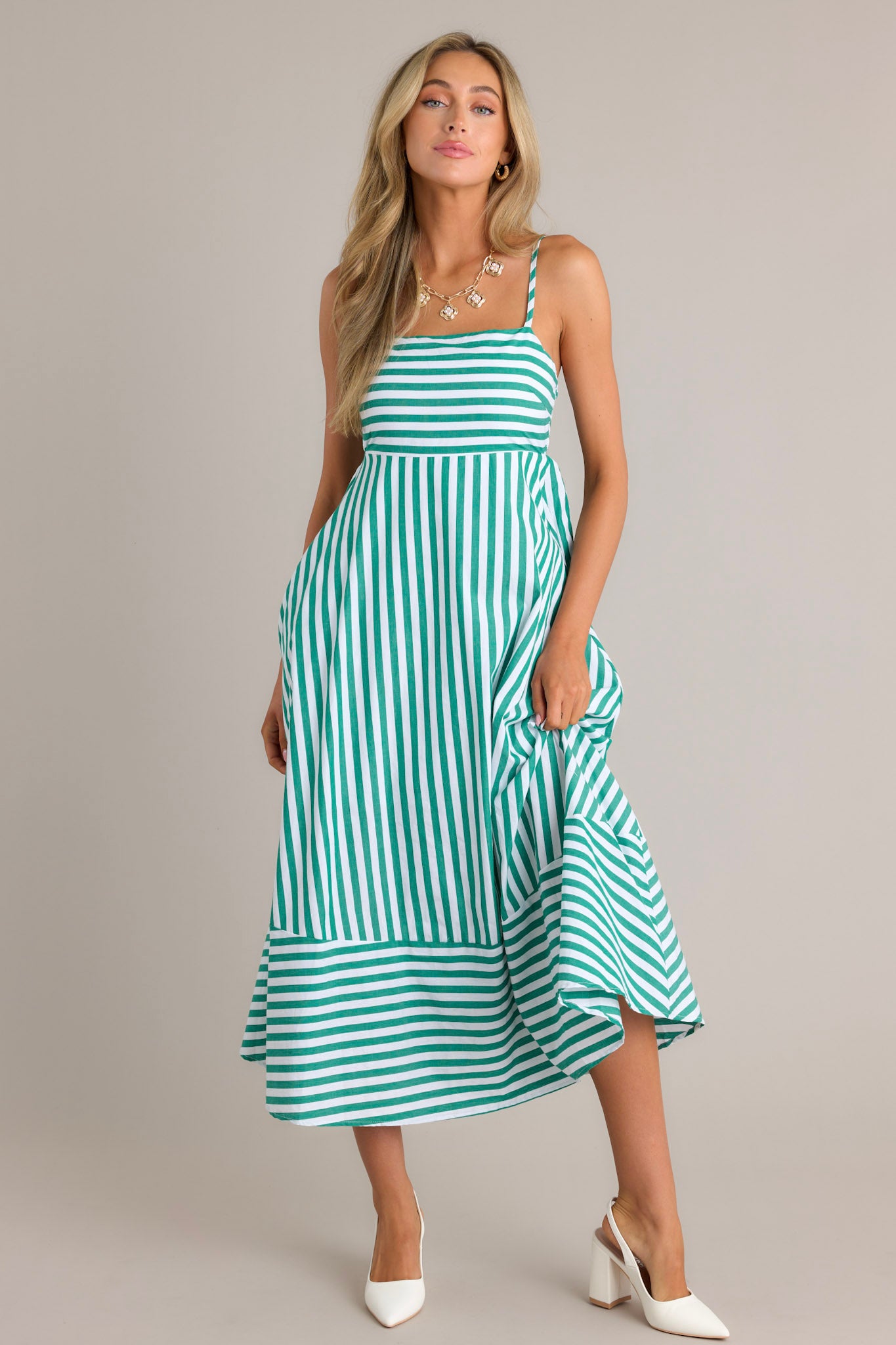 Full length view of a green stripe midi dress with a square neckline, thin adjustable straps, a smocked back insert, functional hip pockets, and horizontal & vertical stripes