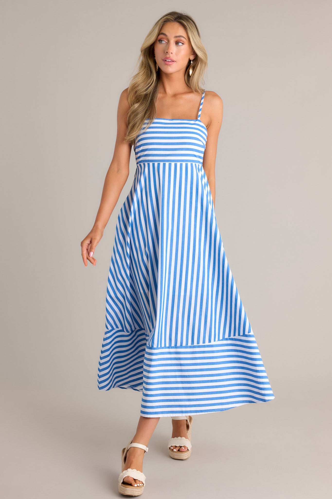 Side view of a blue midi dress showcasing the square neckline, thin adjustable straps, smocked back insert, functional hip pockets, and horizontal & vertical stripes.