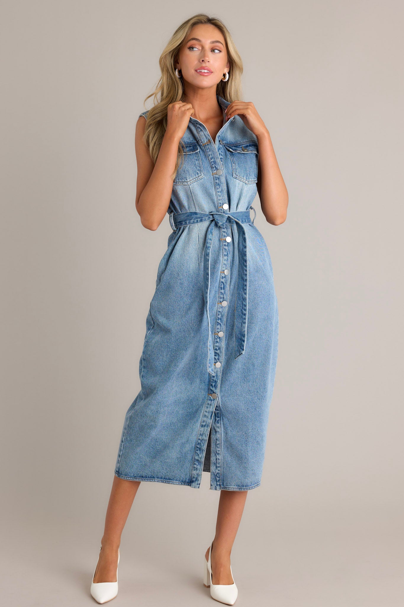 Action shot of a denim maxi dress displaying the flow and movement of the fabric, highlighting the collared neckline, functional button front, functional breast pockets, self-tie waist belt, belt loops, functional hip pockets, and the sleeveless design.