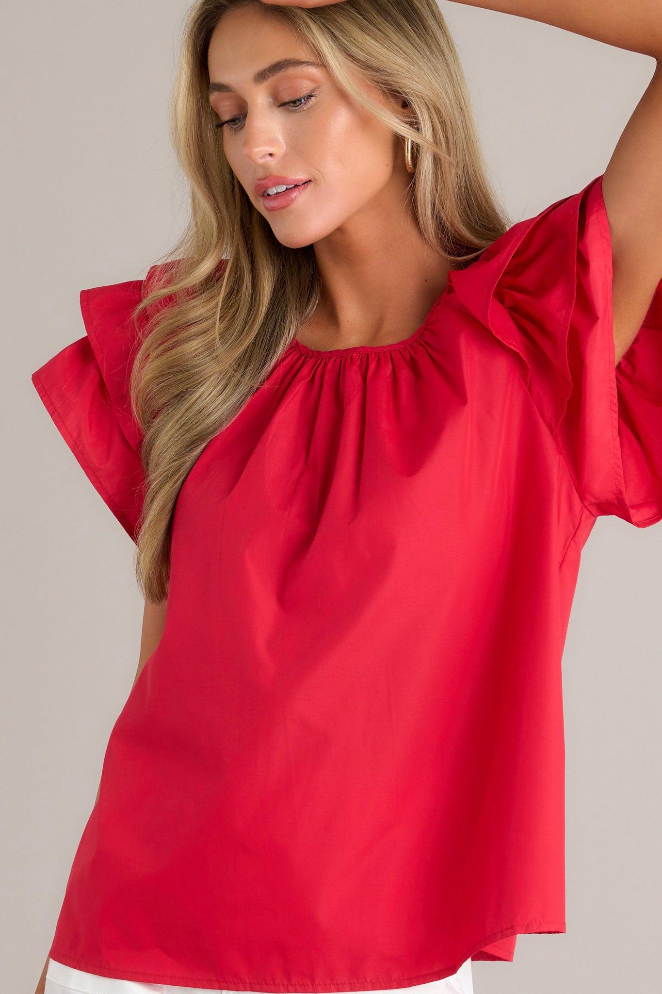 Side view of a red top showcasing the rounded neckline, gathering at the neckline, keyhole with a button closure, and ruffled short sleeves.