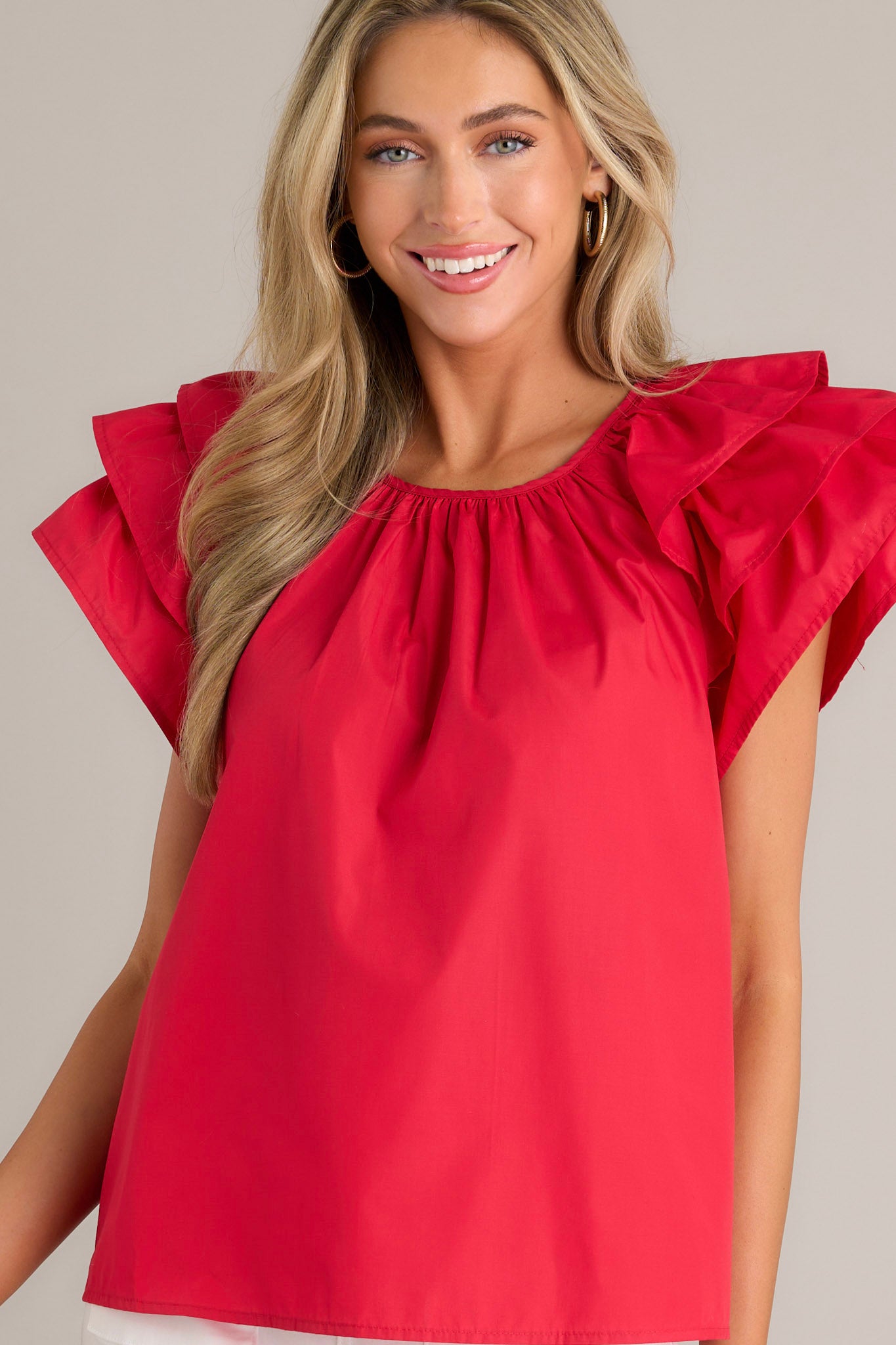 Front view of a red top featuring a rounded neckline, gathering at the neckline, a keyhole with a button closure, and ruffled short sleeves.