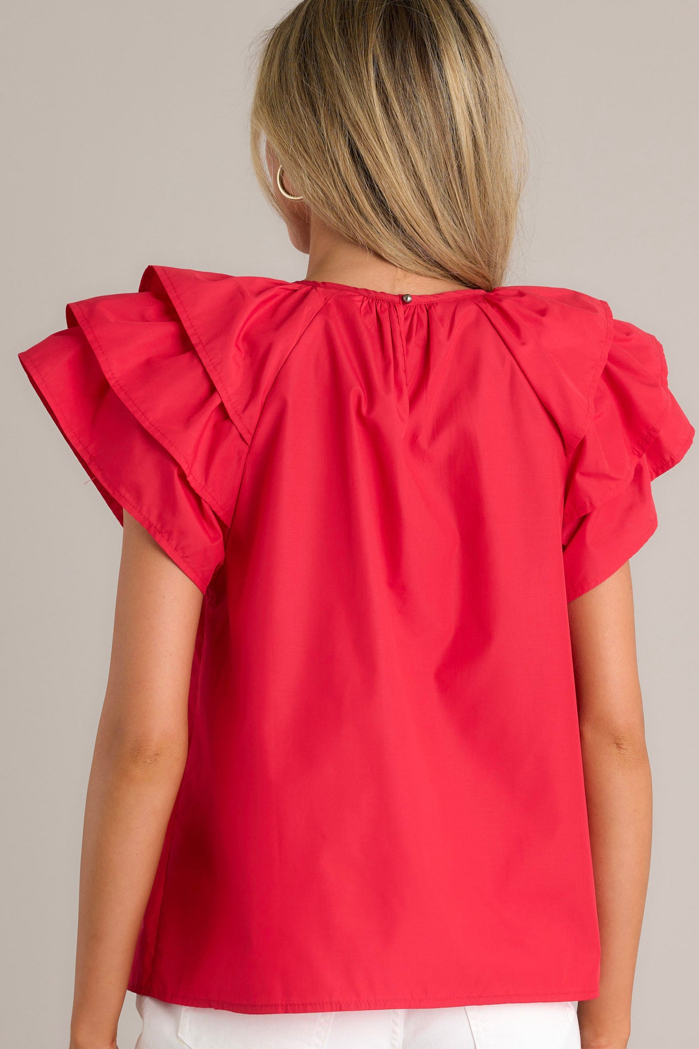 Back view of a red top highlighting the keyhole with a button closure and the ruffled short sleeves.