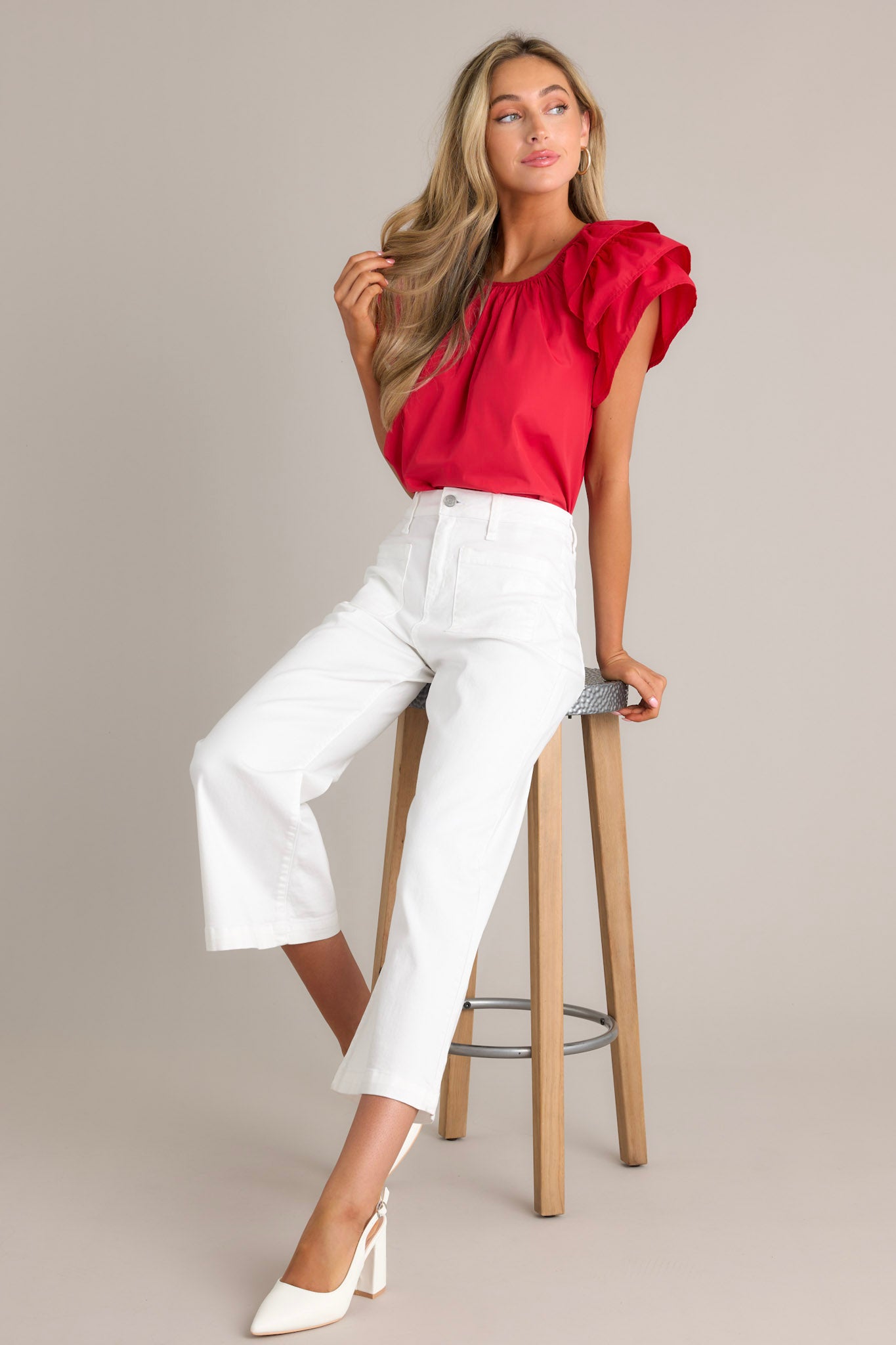 Seated Full length view of white jeans with a high waisted design, a button & zipper closure, belt loops, functional front & back pockets, a cropped hemline, and a flared leg