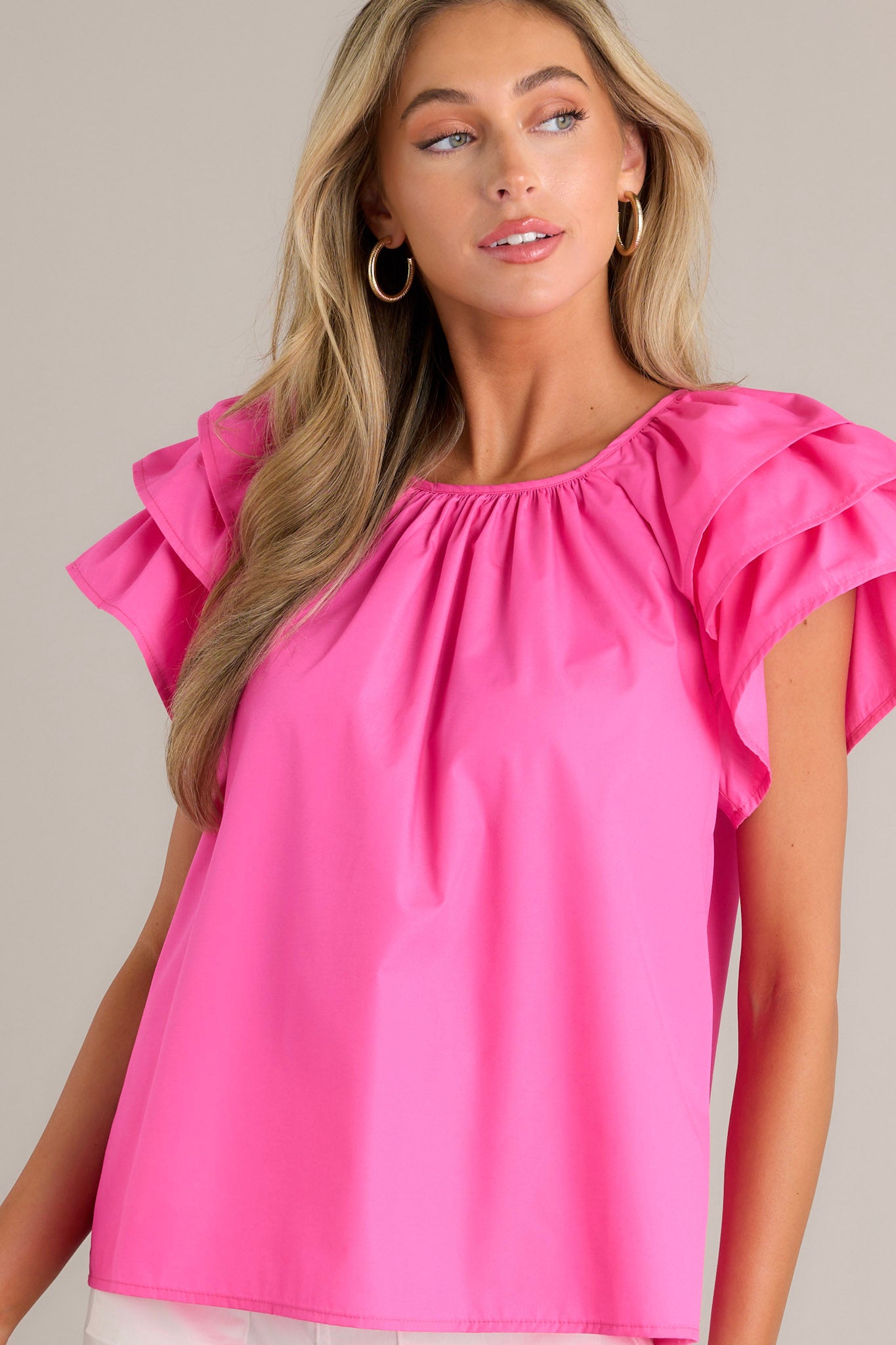 Action shot of a hot pink top displaying the fit and movement, highlighting the rounded neckline, gathering at the neckline, keyhole with a button closure, and ruffled short sleeves.