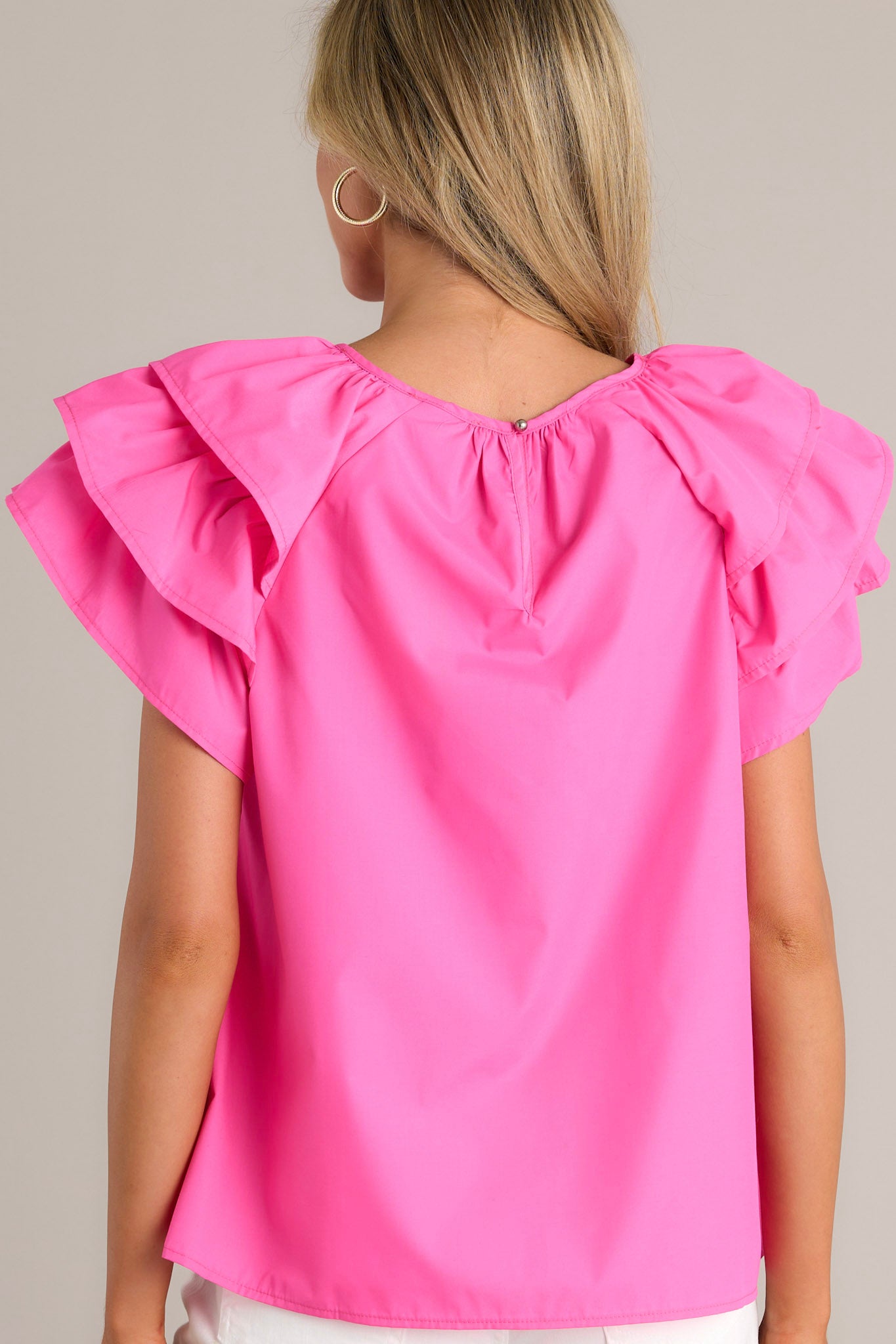 Back view of a hot pink top highlighting the overall fit, rounded neckline, and ruffled short sleeves.