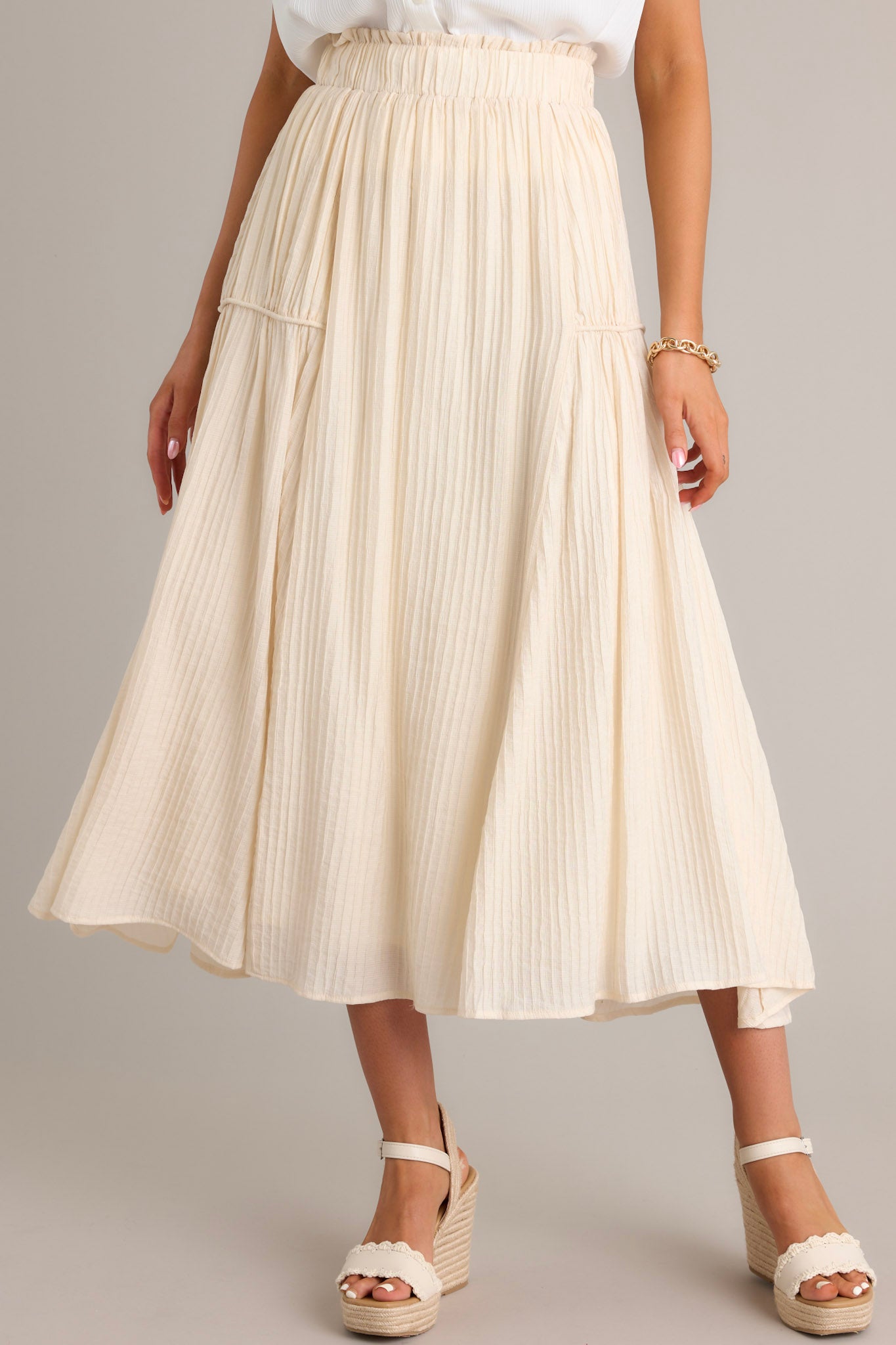 Front view of a beige maxi skirt featuring a high waist design, an elastic waistband, a ribbed texture, and a flowing silhouette.