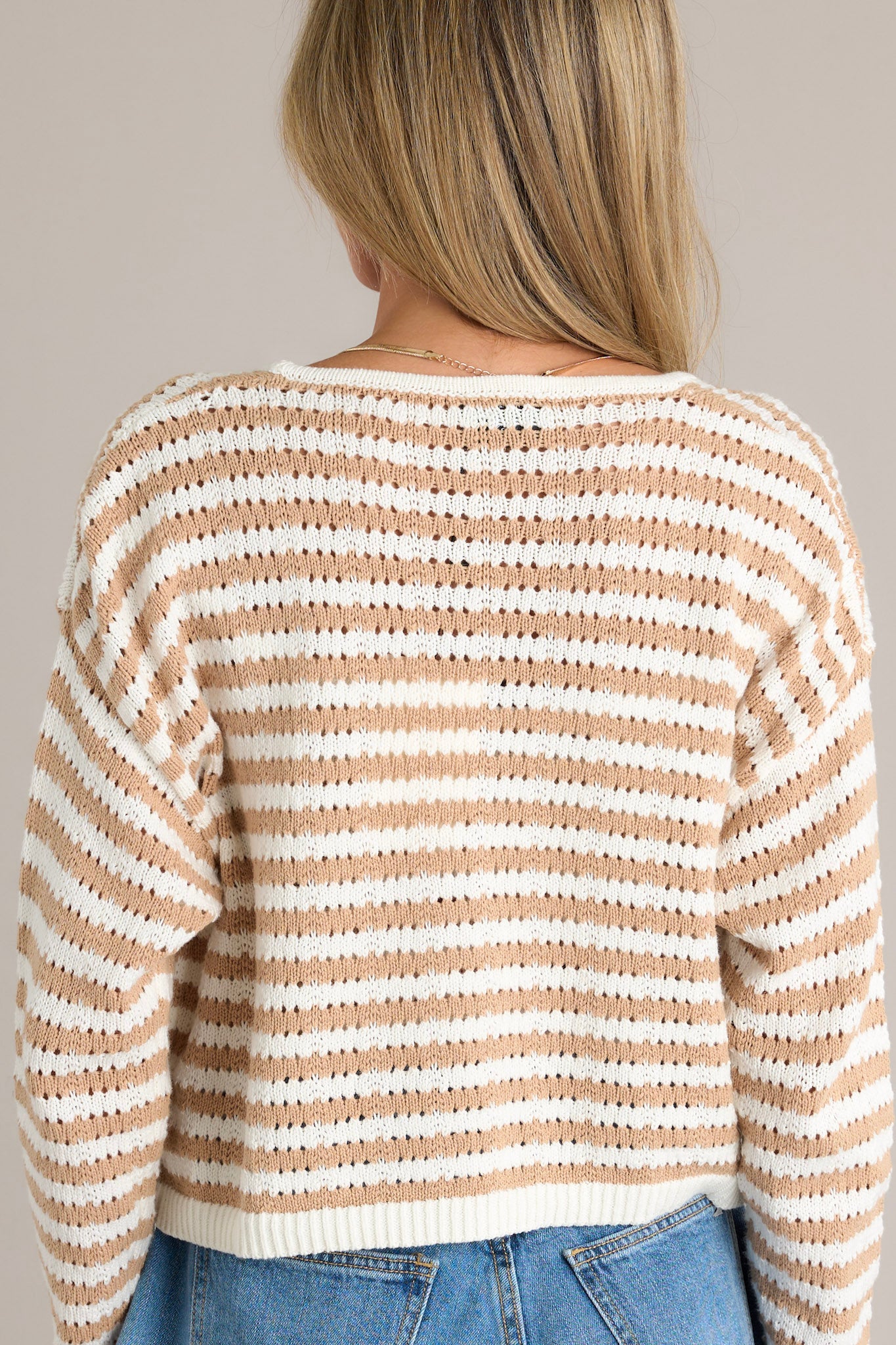 Back view of a tan stripe cardigan highlighting the open knit design and the cropped hemline.