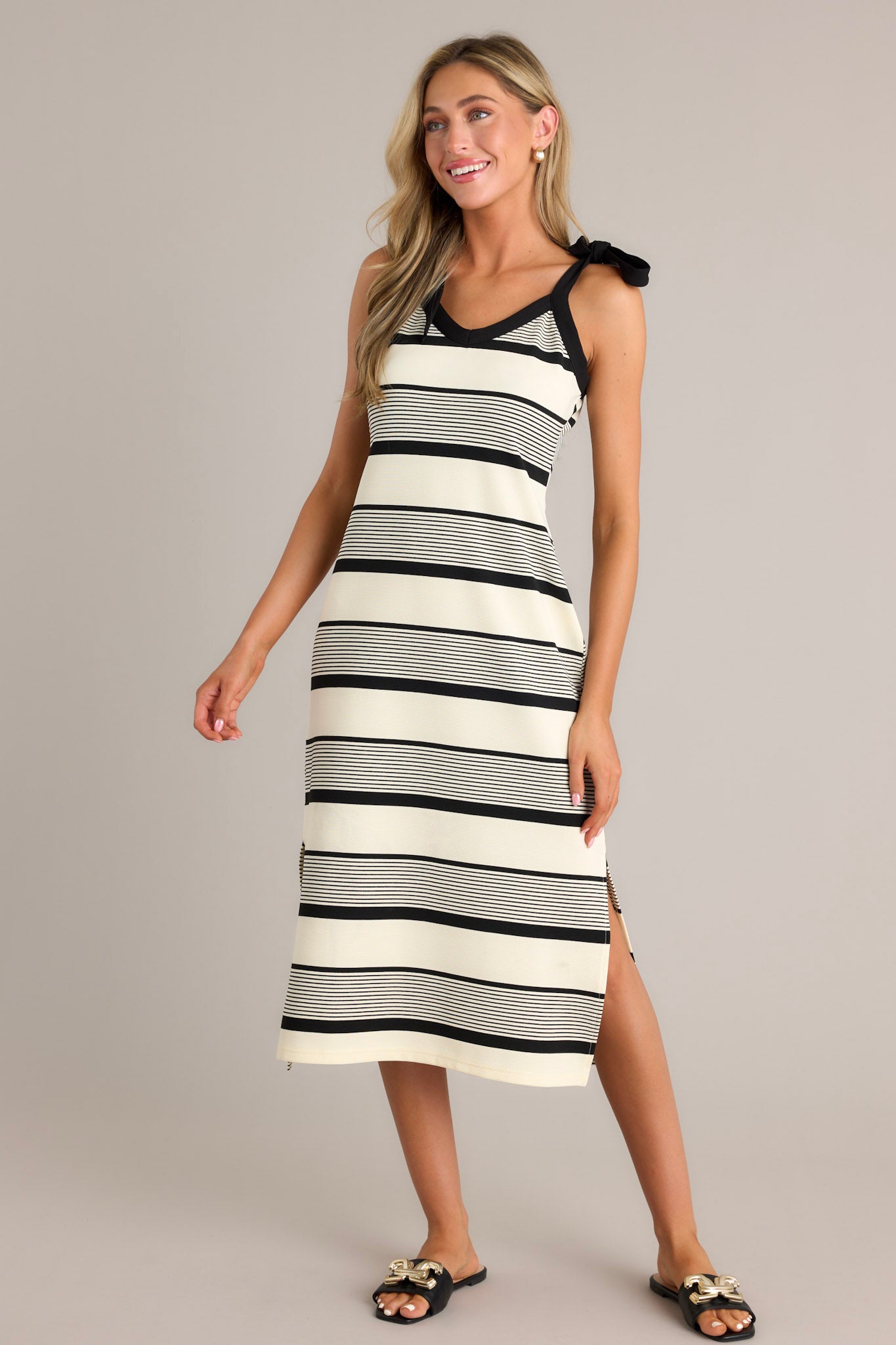 Action shot of a black striped midi dress displaying the fit and movement, highlighting the v-neckline, thick self-tie straps, unique stripe pattern, and side slits.