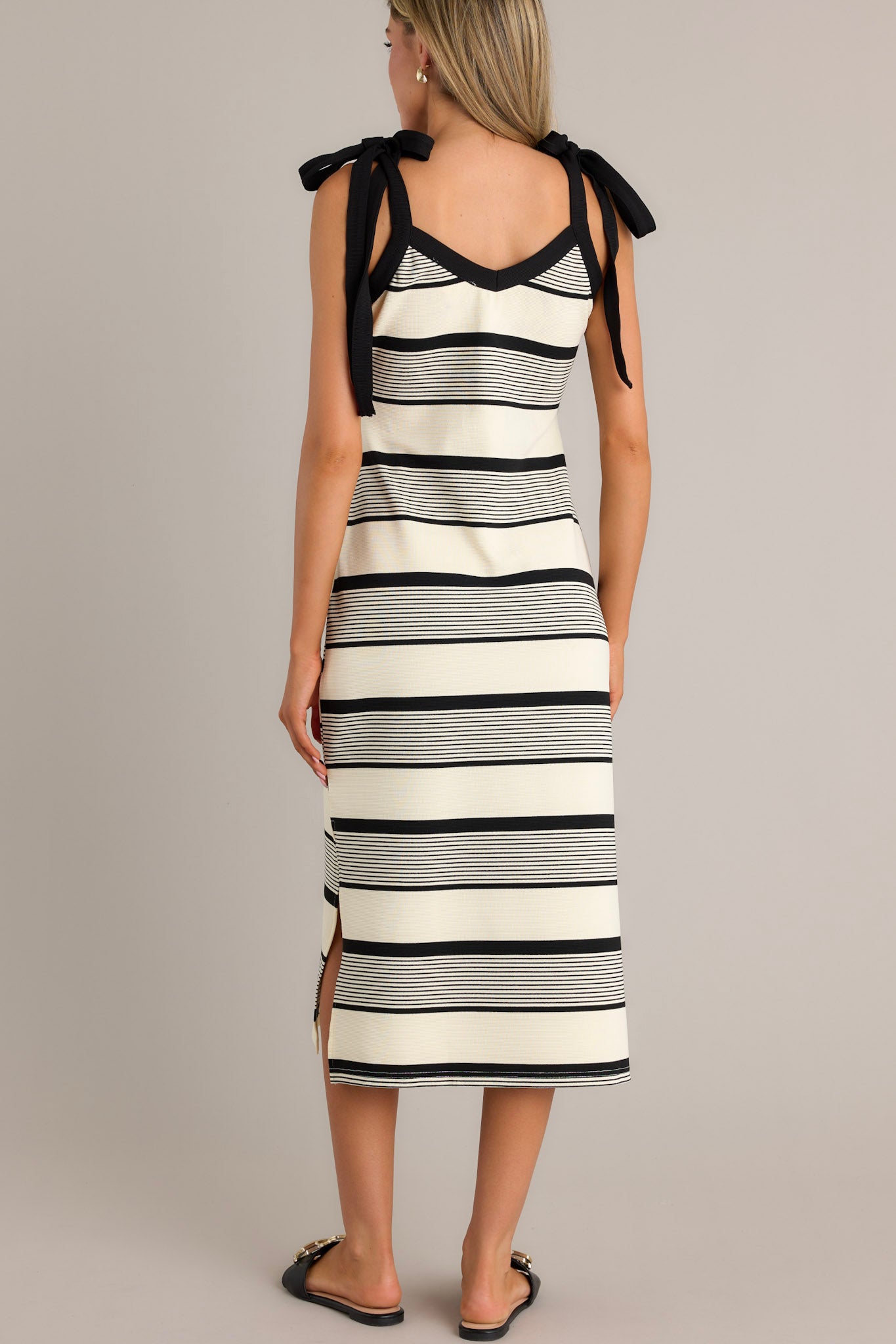 Back view of a black striped midi dress highlighting the thick self-tie straps, unique stripe pattern, and side slits.
