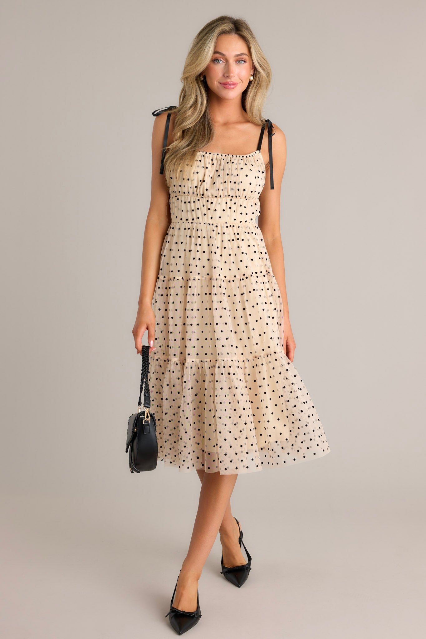 This beige midi dress features a square neckline, thin self-tie straps, an elastic waistline, tiers, black polka dots, and tulle.