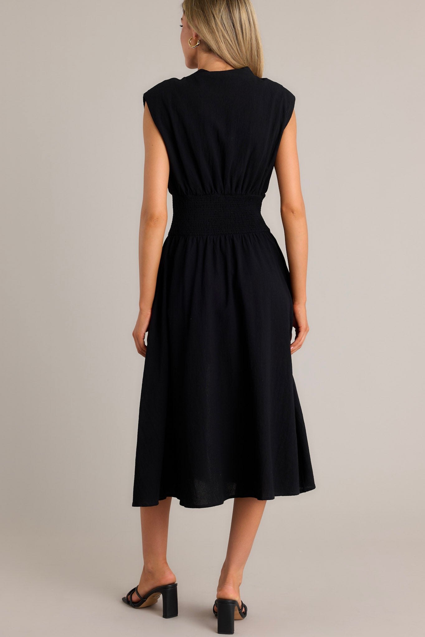 Back view of a black midi dress highlighting the shoulder padding, fully smocked waist, and overall fit.