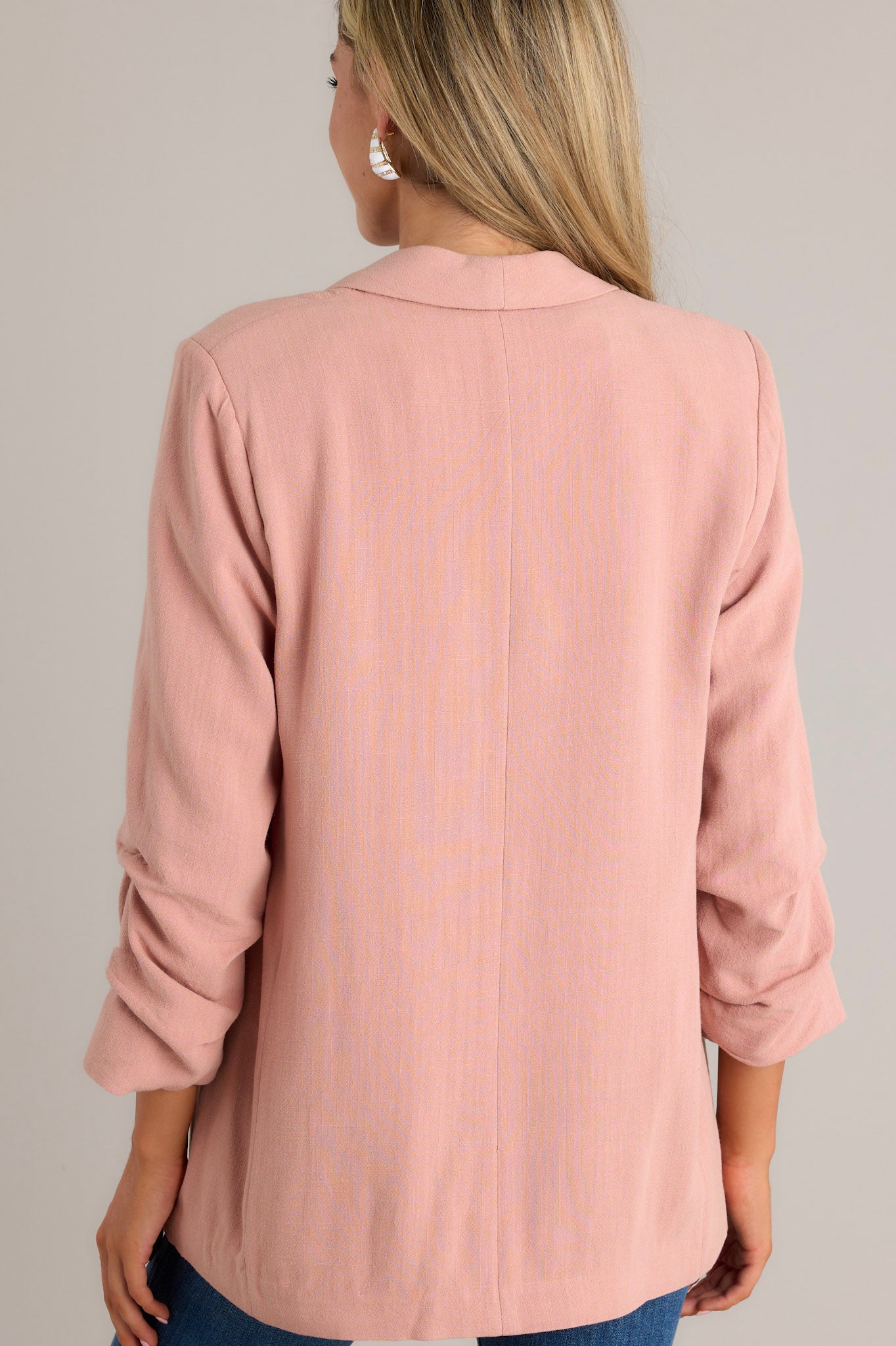 Back view of this dusty rose blazer featuring a folded neckline, shoulder padding, faux pockets, and gathering in the quarter-length sleeves.