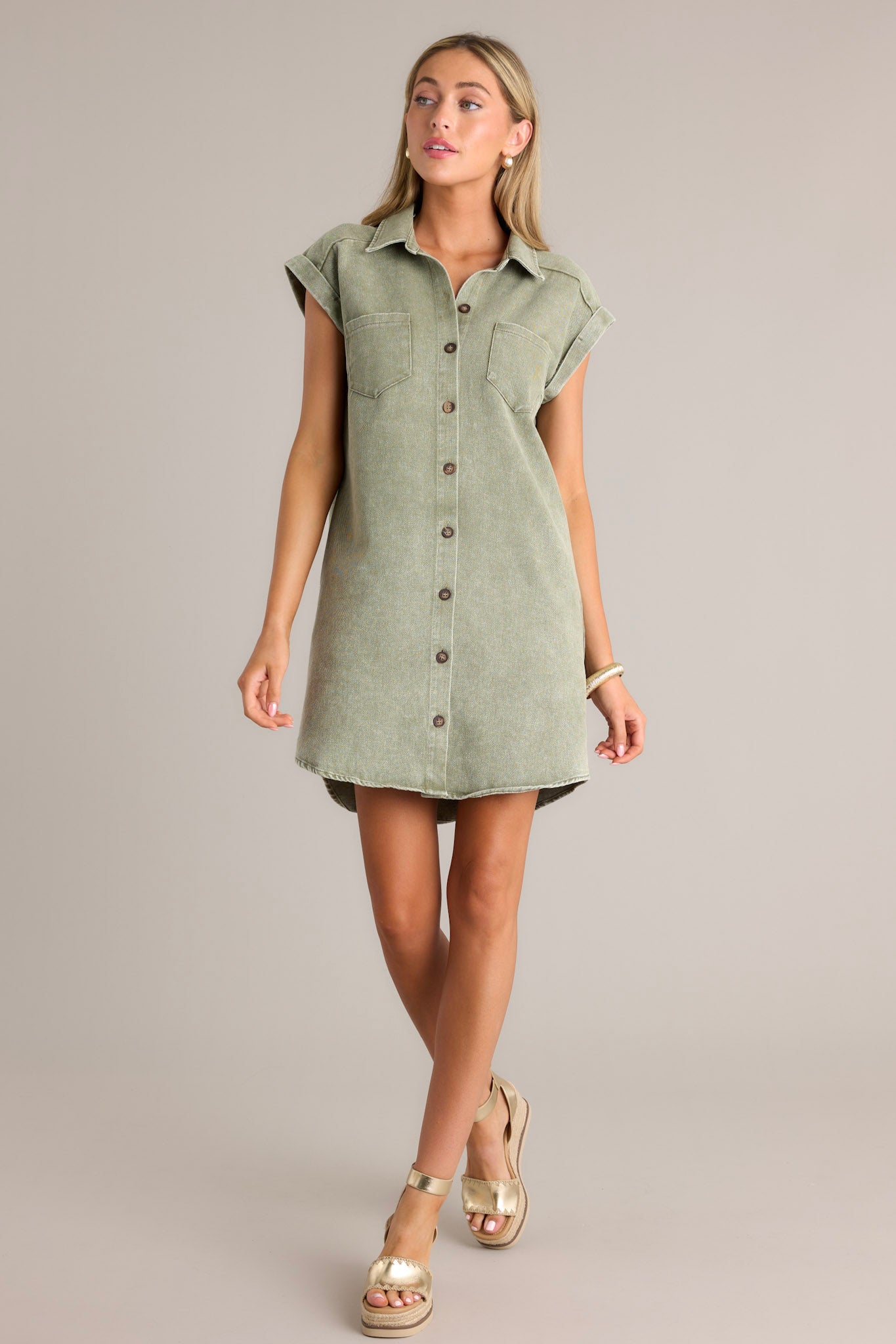 Front angled view of a green mini dress featuring a collared neckline, a full button front, functional breast & hip pockets, and folded short sleeves