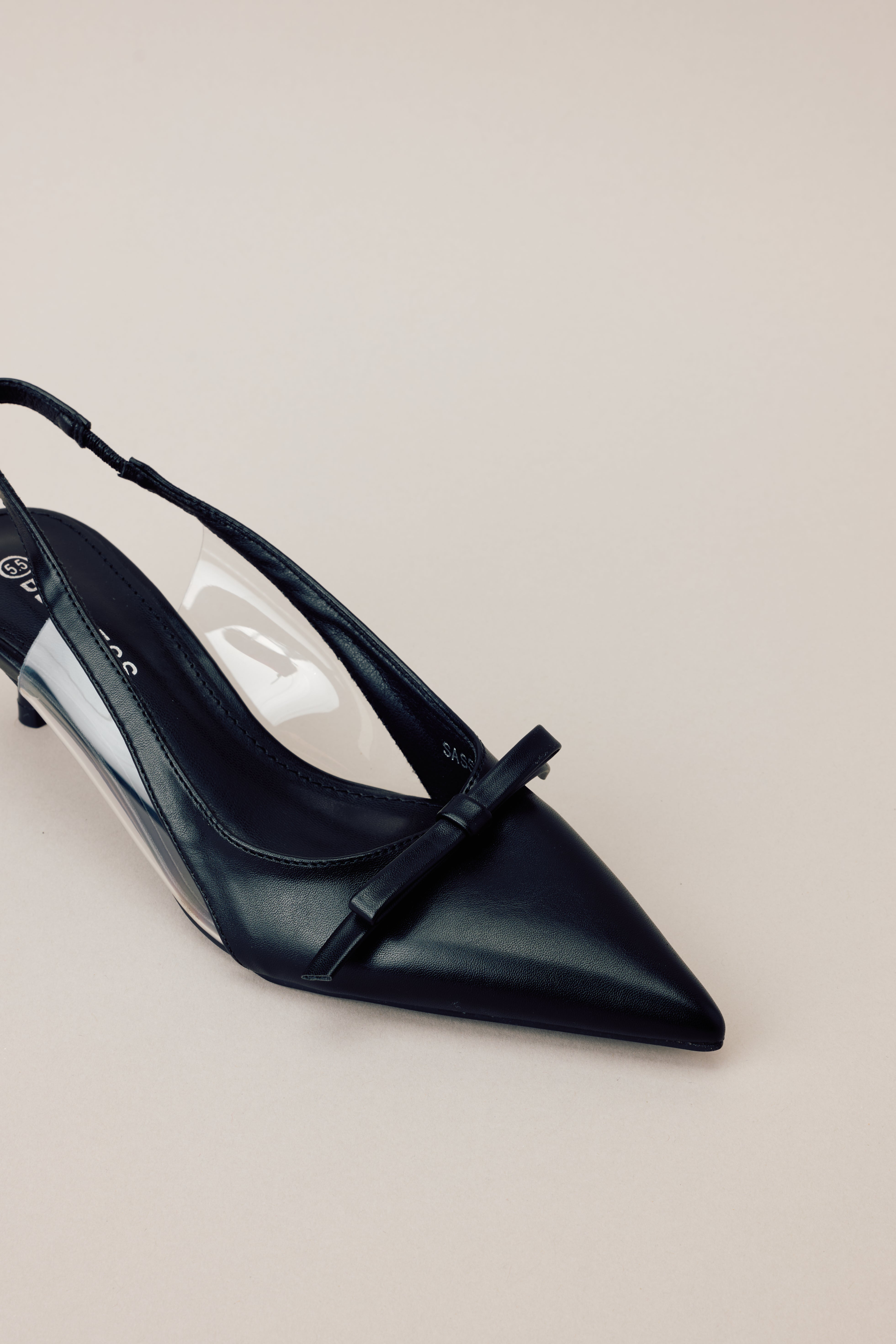 Close-up of the black kitten heels showing the pointed closed toe, delicate bow detailing, and clear siding for extra support.