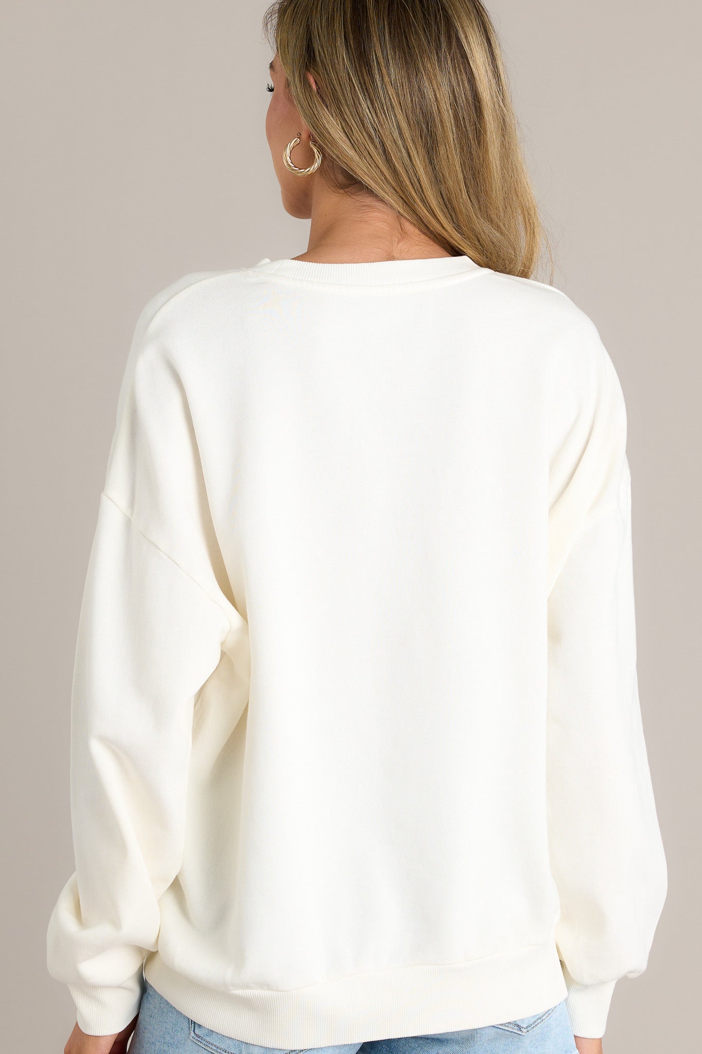 Back view of a white sweatshirt highlighting the overall fit and ribbed cuffed long sleeves.