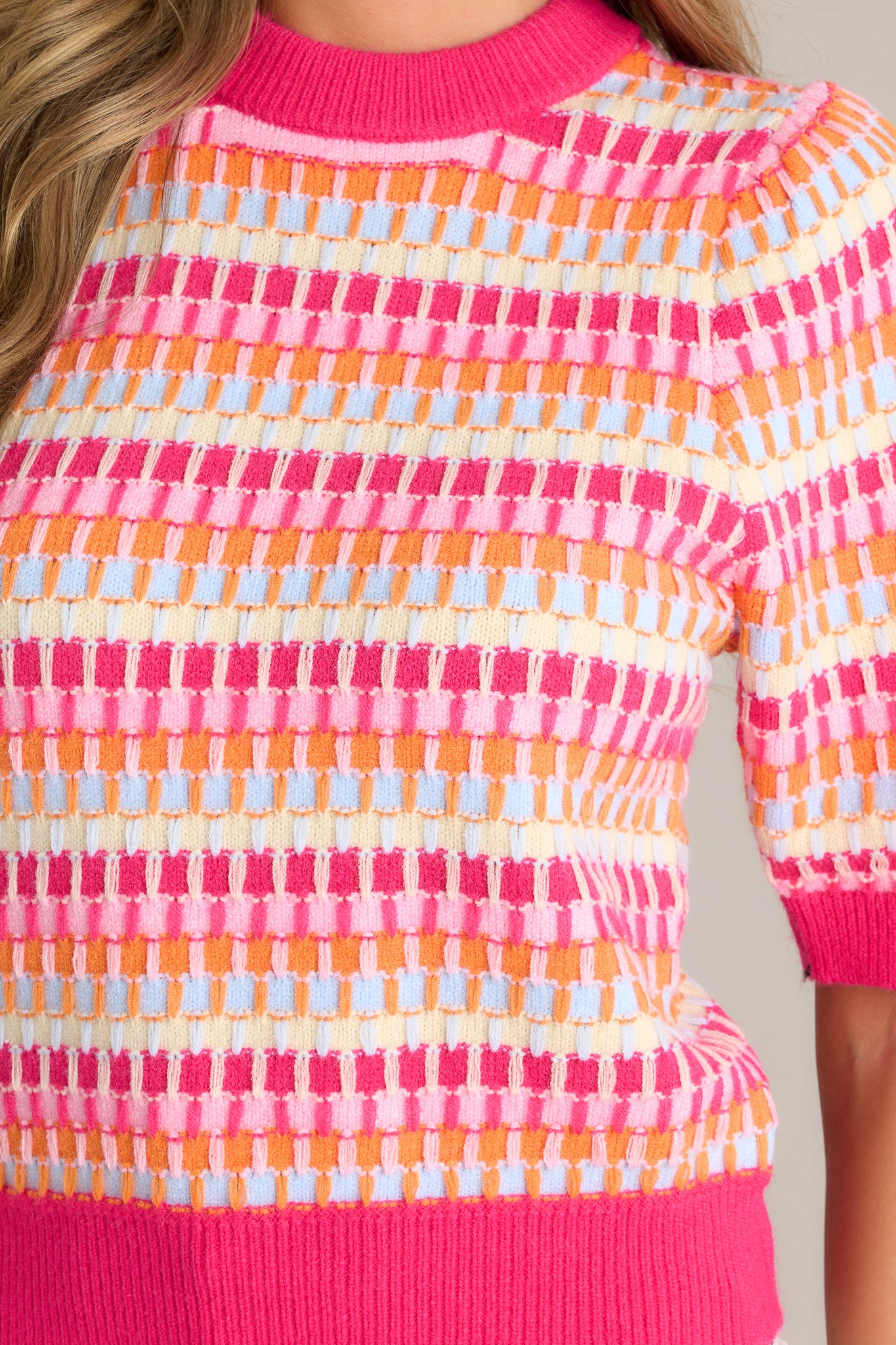 Close-up of the pink stripe sweater showing the ribbed crew neckline, multicolored knitted stripes, and ribbed cuffed half sleeves.