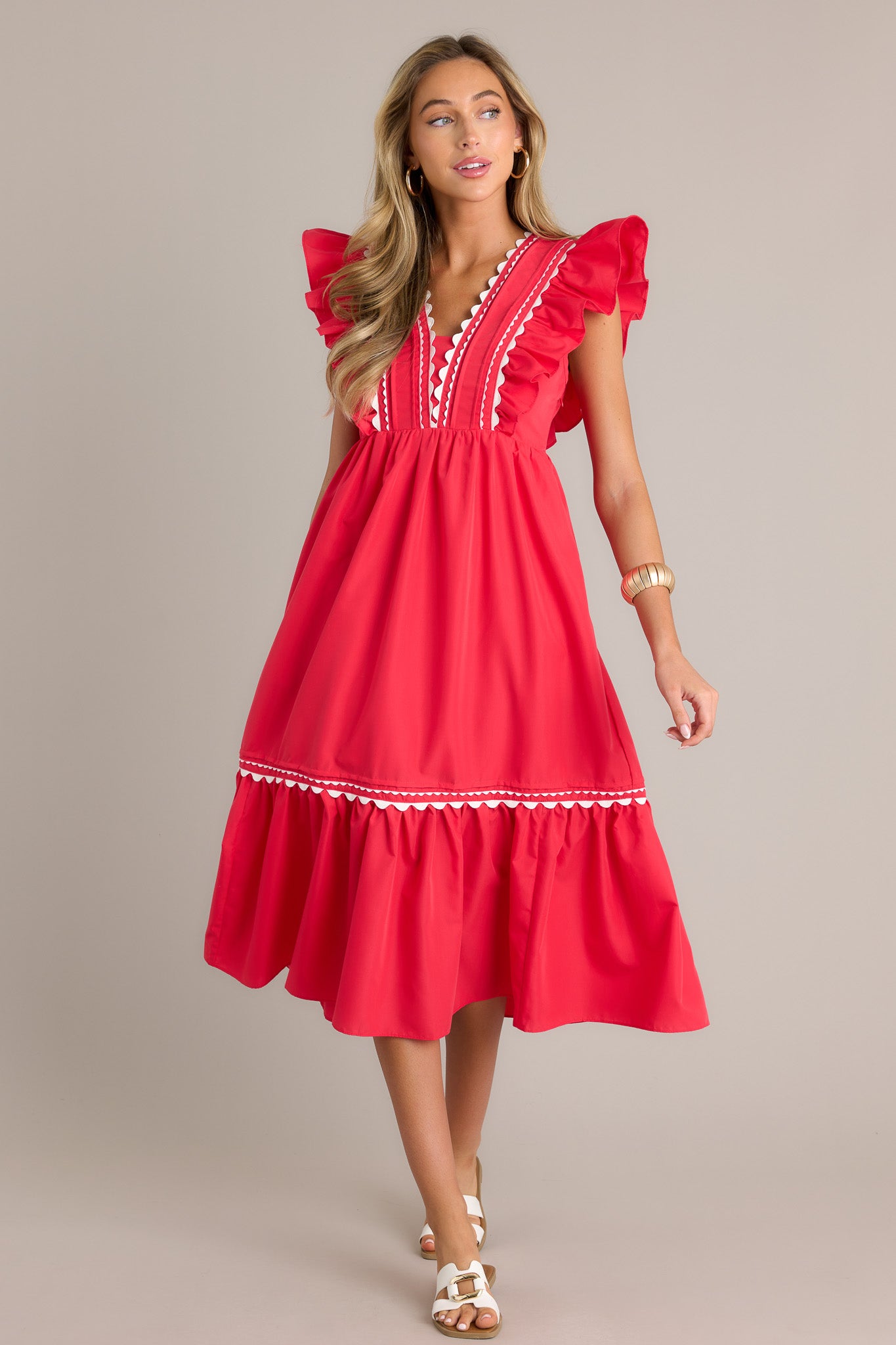 Action shot of a red midi dress displaying the fit and movement, highlighting the v-neckline, scalloped and ruffled bodice detailing, functional hip pockets, and short flutter sleeves.