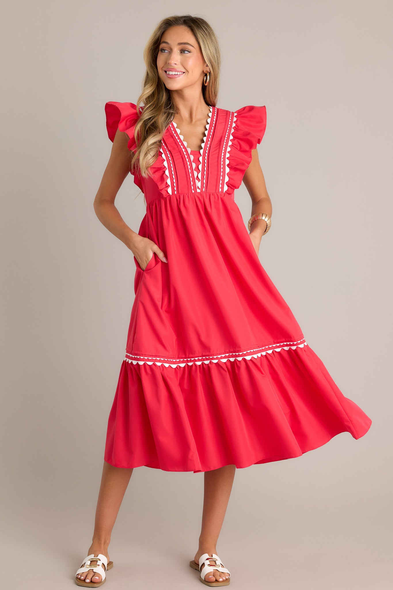 Front view of a red midi dress featuring a v-neckline, scalloped and ruffled bodice detailing, functional hip pockets, and short flutter sleeves.