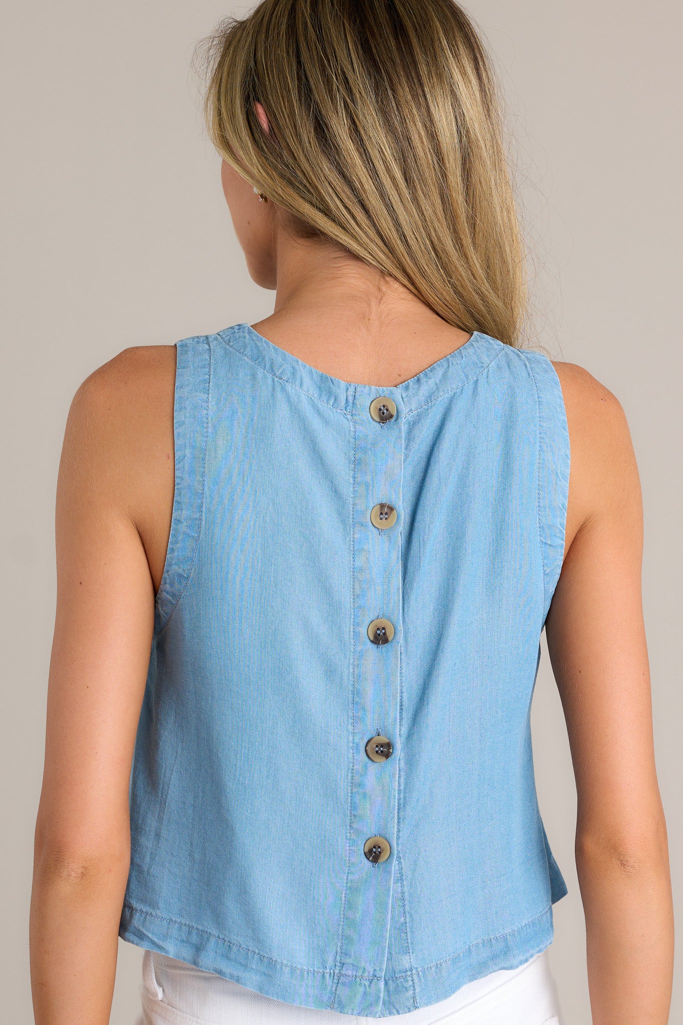 Back view of a chambray tank top highlighting the functional buttons down the back, sleeveless design, and overall fit.