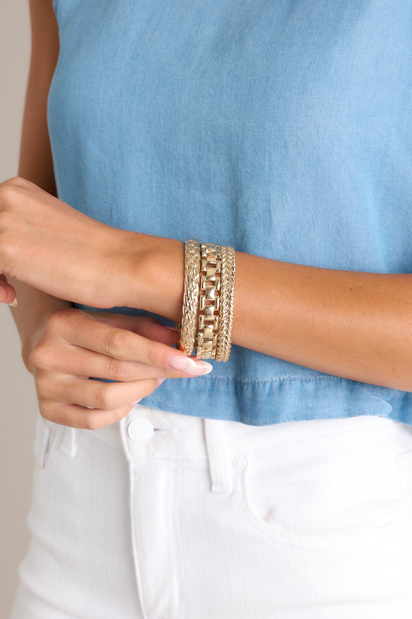 These gold bangles feature gold hardware, two bangles with a braided design, and one bangle with a chain-like design.