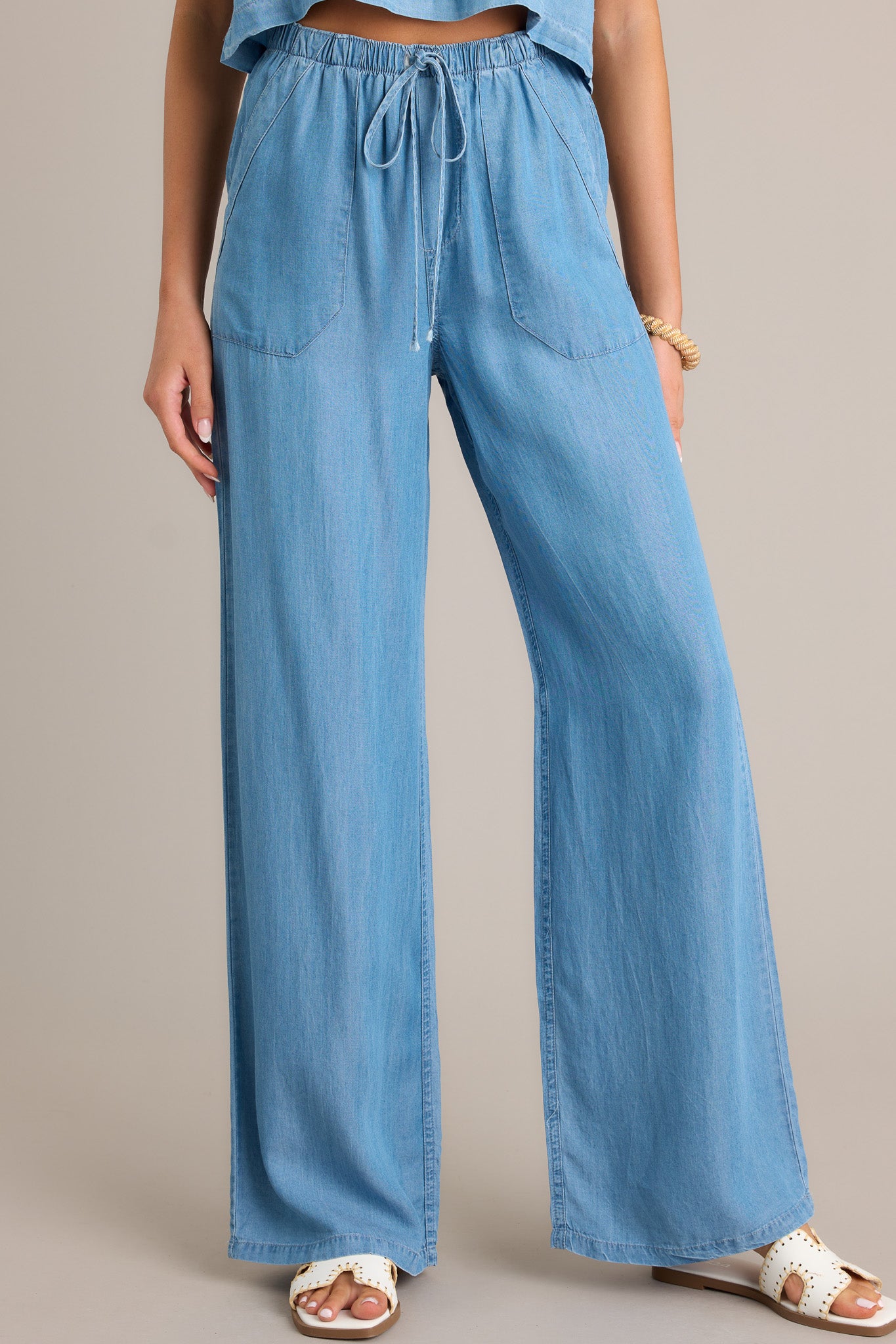 Front angled view of chambray pants featuring an elastic waistband, a self-tied drawstring, functional front and back pockets, and a wide leg