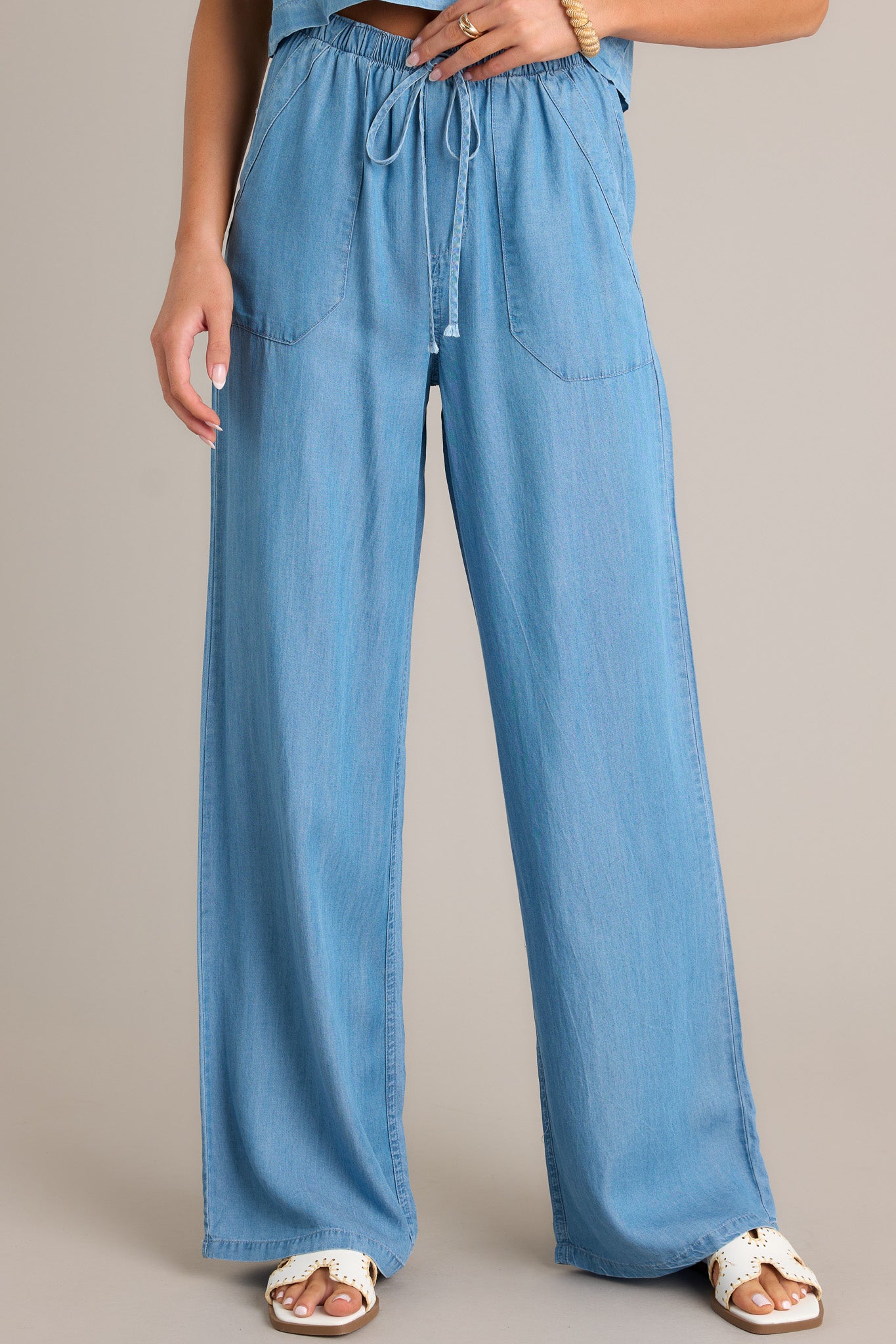 Front view of chambray pants featuring an elastic waistband, a self-tied drawstring, functional front pockets, and a wide leg.