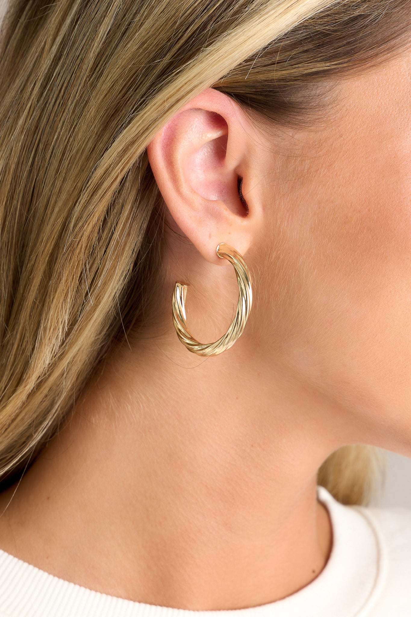 Close up view of These earrings feature gold hardware, a twist like design, and a secure post backing.