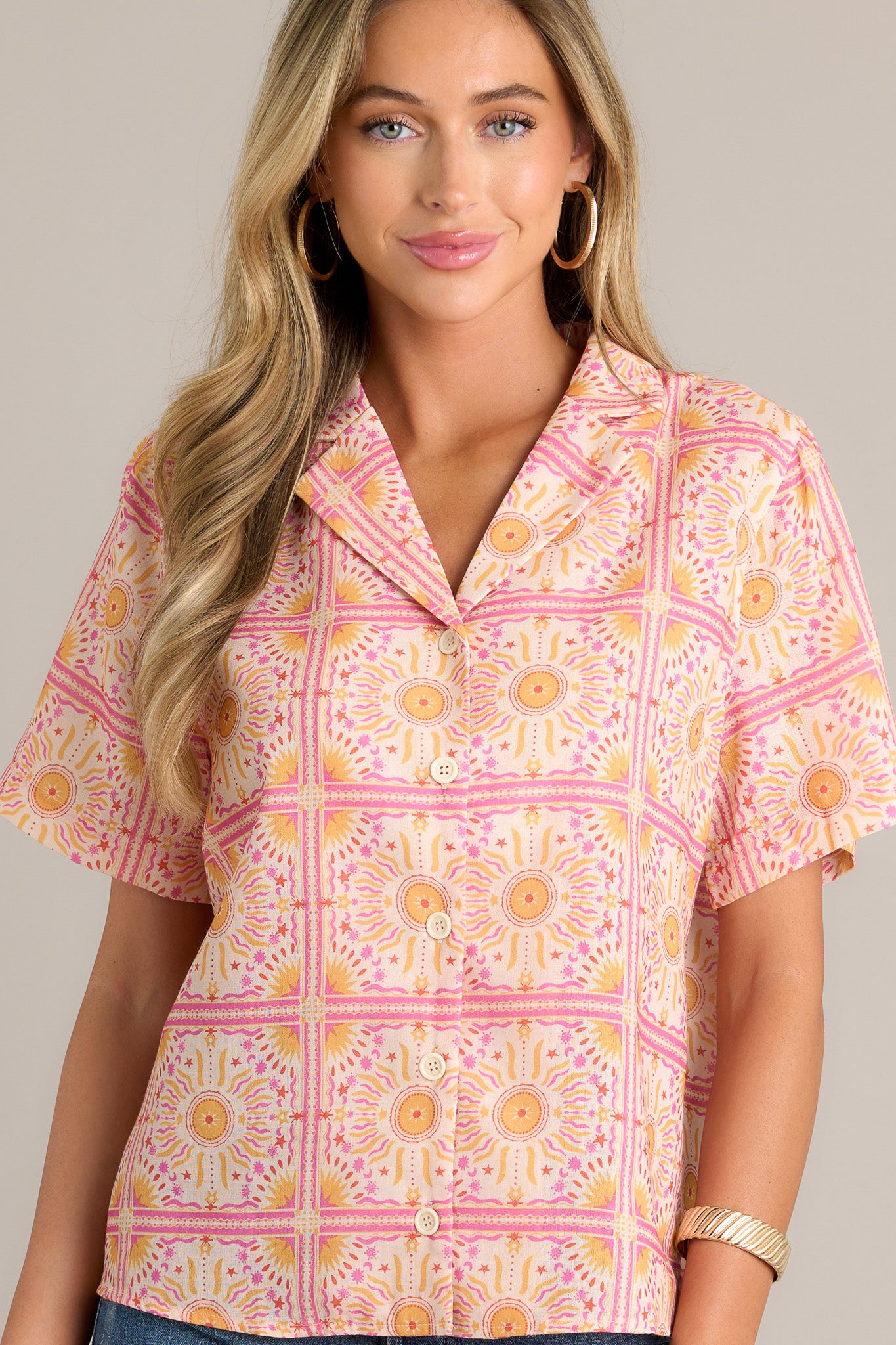 Front view of a pink top featuring a notched lapel collared neckline, a full button front, a relaxed fit, short sleeves, and a fun and unique print.